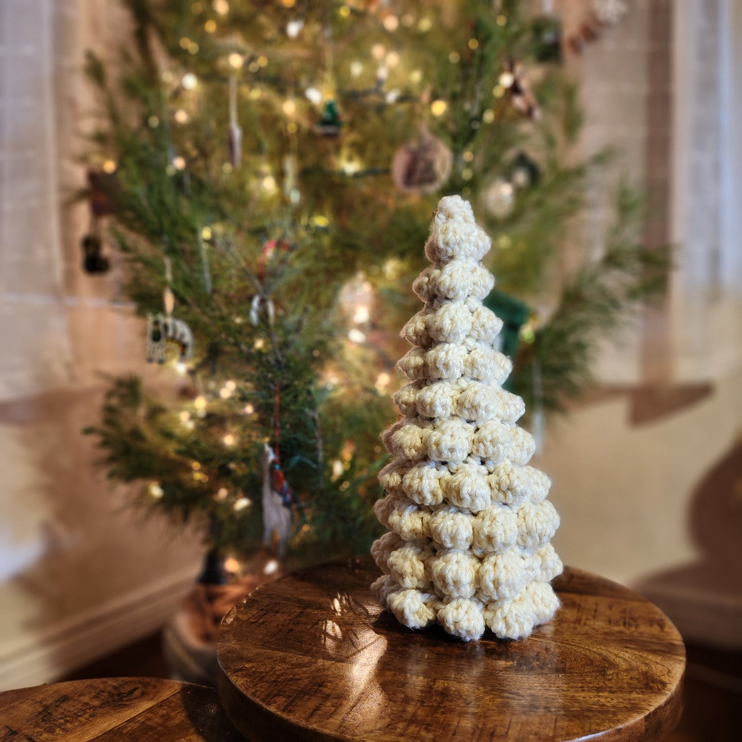 Hand crocheted wine bottle covers in various colors designed to resemble Christmas trees, displayed in front of a blurred Christmas tree background.