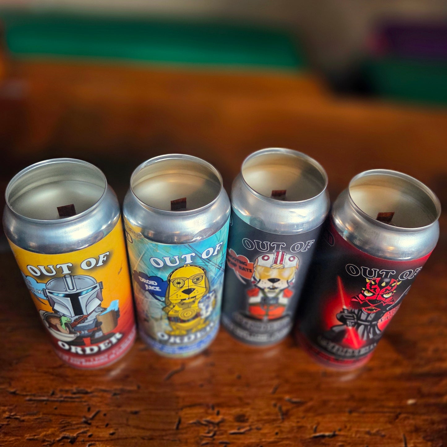 A set of four Star Wars-inspired beer can candles lined up on a wooden surface, each featuring a wooden wick and character artwork from the RaR Brewing "Out of Order" series—designed as humorous canine versions of popular sci-fi figures.