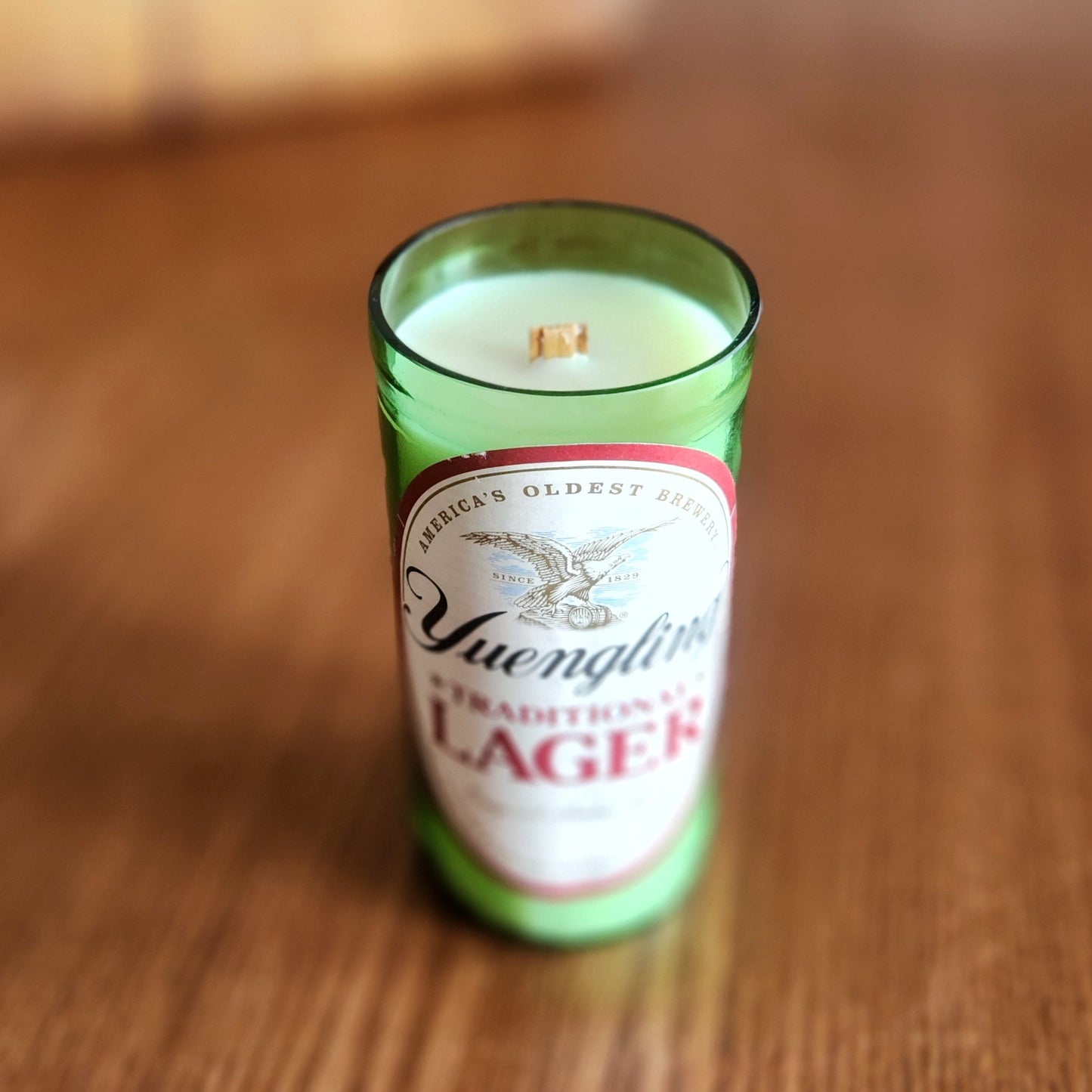 Angled view of a Yuengling beer bottle candle with a clean wooden wick and creamy coconut soy wax. The recycled green glass vessel features the iconic Yuengling label, now transformed into an eco-friendly, hand-poured candle.