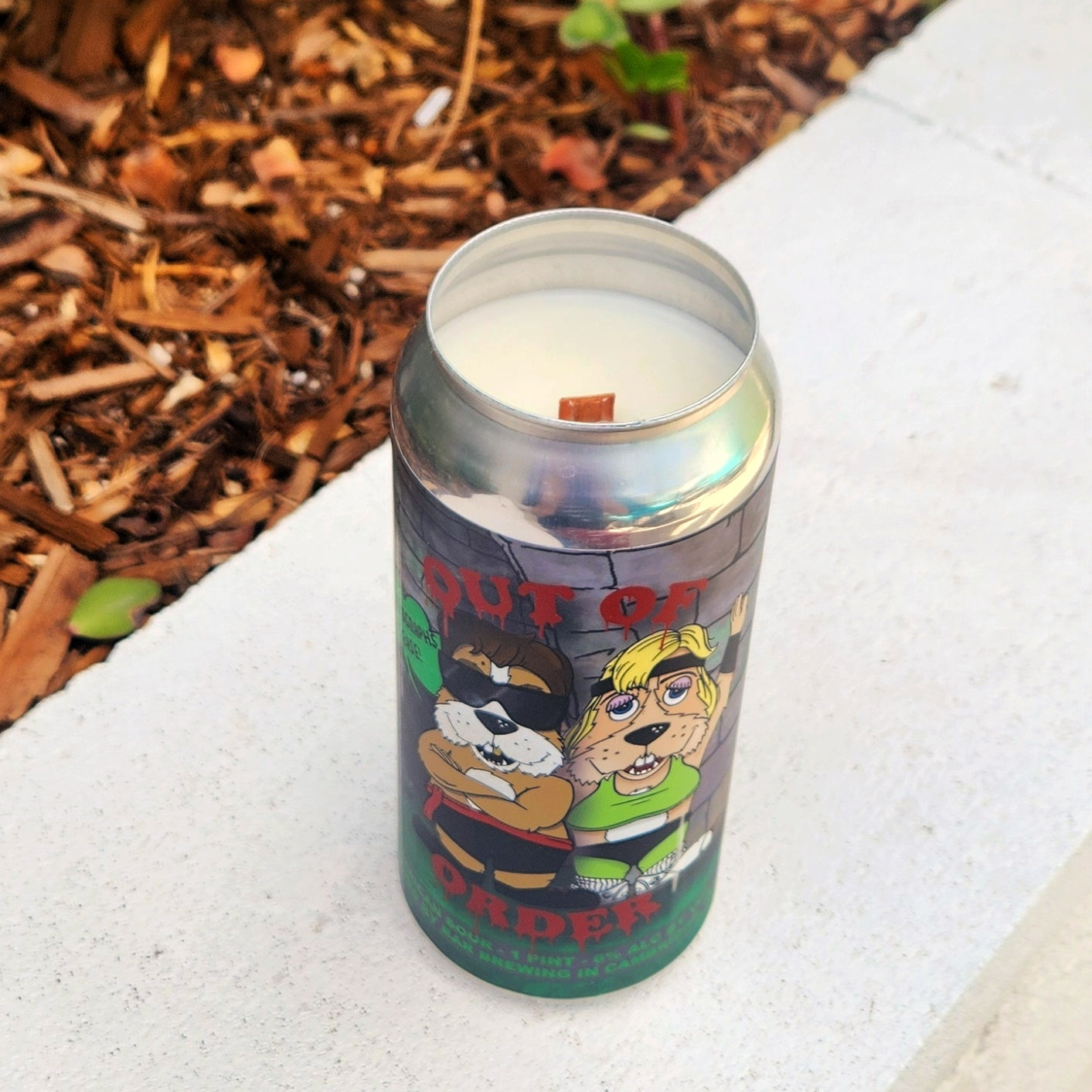 Eco-friendly coconut soy candle in a recycled RaR Brewing beer can. The label features cartoon-style anthropomorphic dogs dressed in parody Mortal K costumes against a stone wall. Bold red text reads “Out of Order,” and the wooden wick peeks through the creamy white wax.