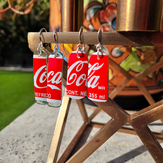 2 pair Coca-Cola bottle earrings on a wooden stand with a blurred outdoor background