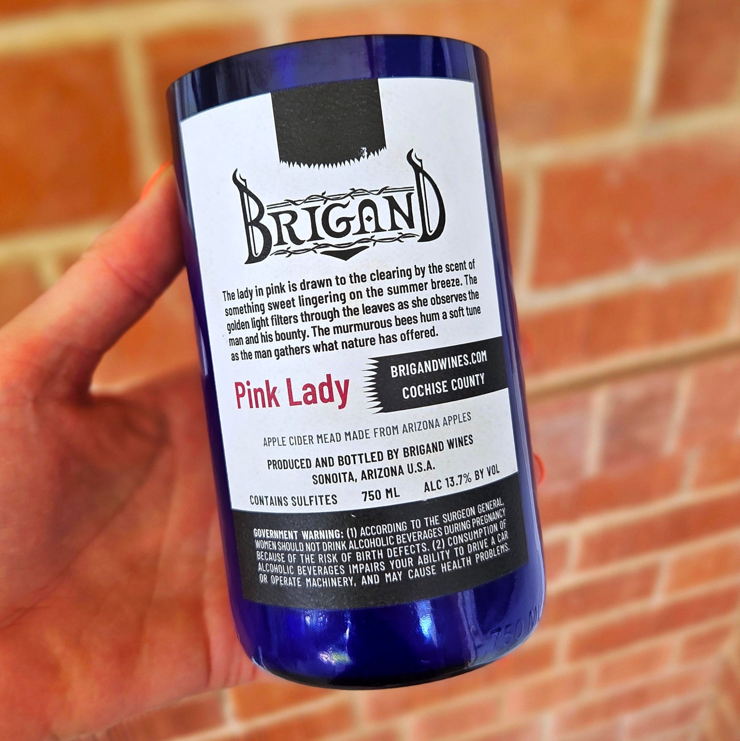 Back view of a recycled blue bottle candle featuring the original Brigand Wines "Pink Lady" label, highlighting its Arizona-made apple cider mead origins and handcrafted, eco-friendly transformation into a coconut soy wax candle.