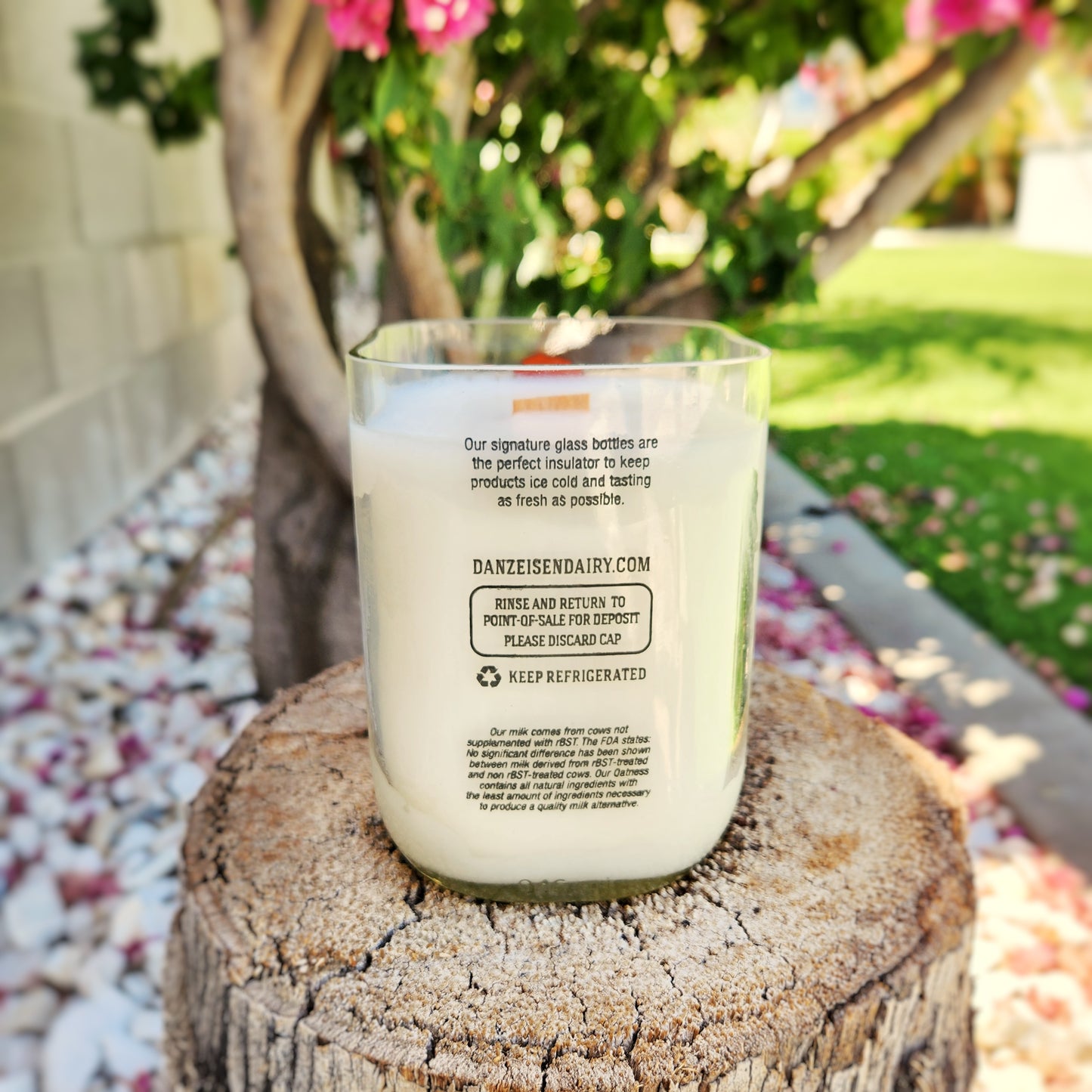 Rear label view of a clean-burning candle made in a repurposed Danzeisen Dairy bottle. Set outdoors on a tree stump, the label details the dairy’s info and highlights the candle’s eco-conscious origin.