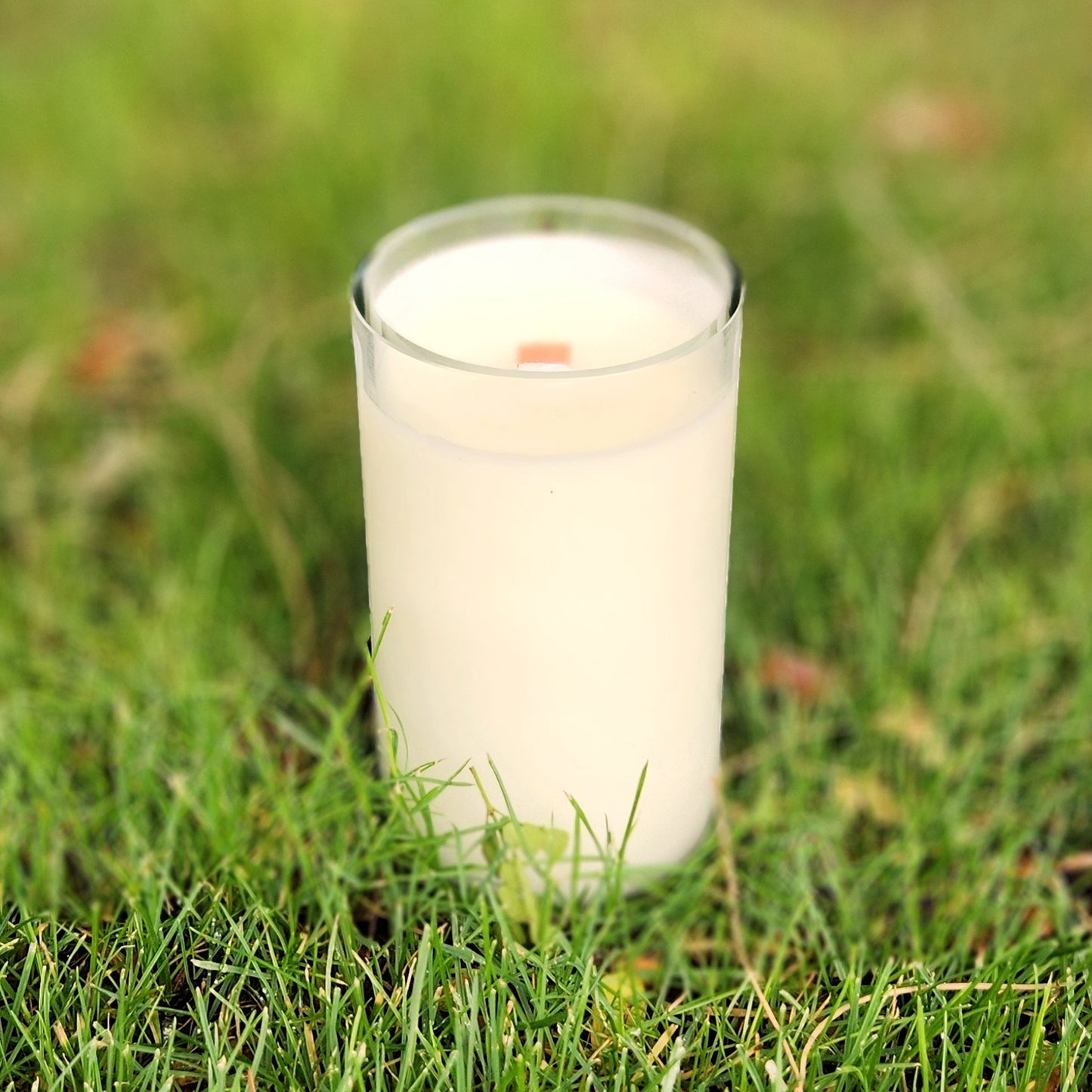 Back view of a hand-poured wine bottle candle made from a recycled Hive Five Meadery bottle with a vibrant Arizona flag label, resting on green grass.