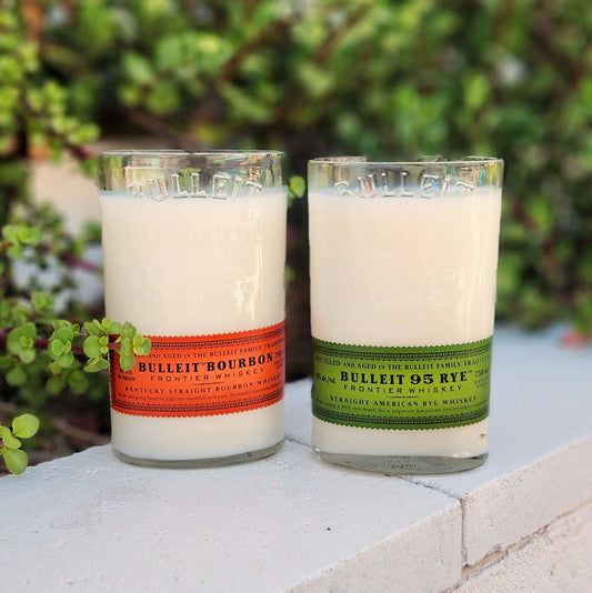 Front-facing view of upcycled Bulleit whiskey bottle candles in green and orange label variants, featuring sustainable coconut soy wax and double wooden wicks for a rustic, clean-burning glow.