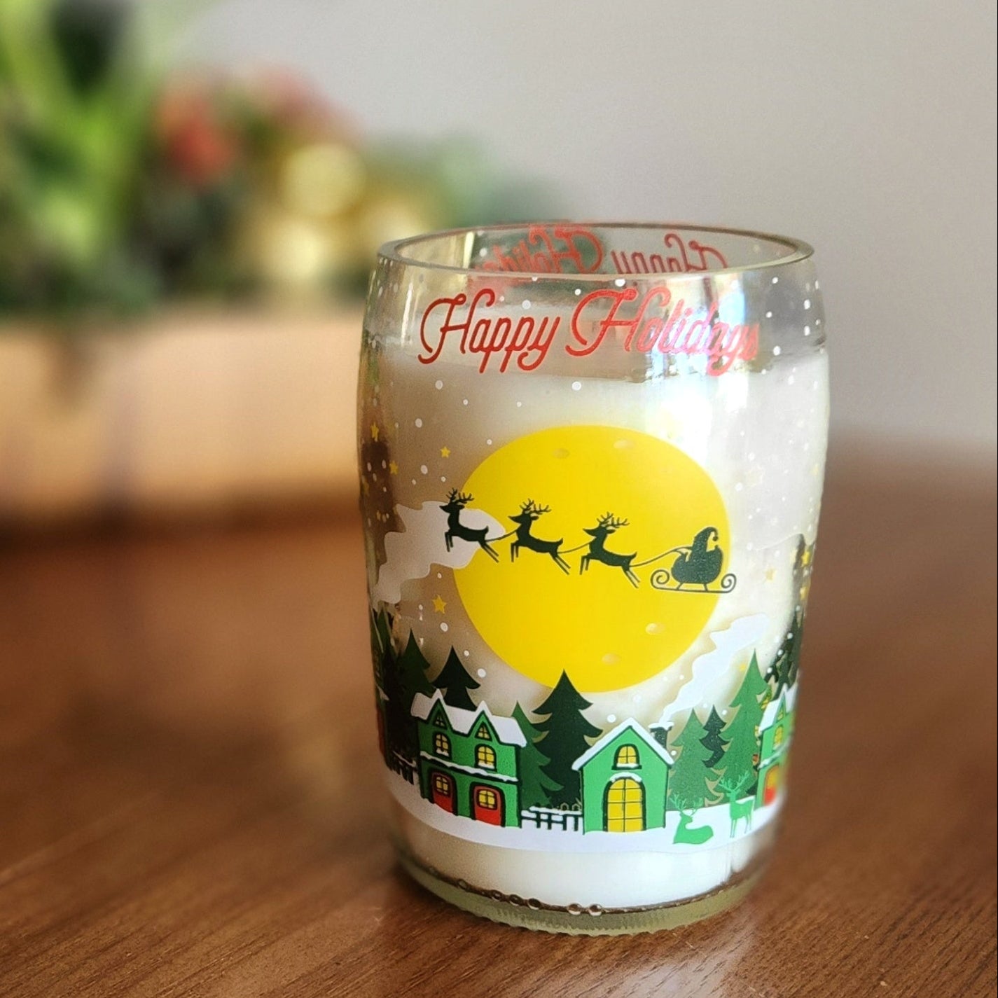 This festive candle, set in a recycled prosecco bottle featuring a charming holiday village and Santa's sleigh, radiates warmth and seasonal magic