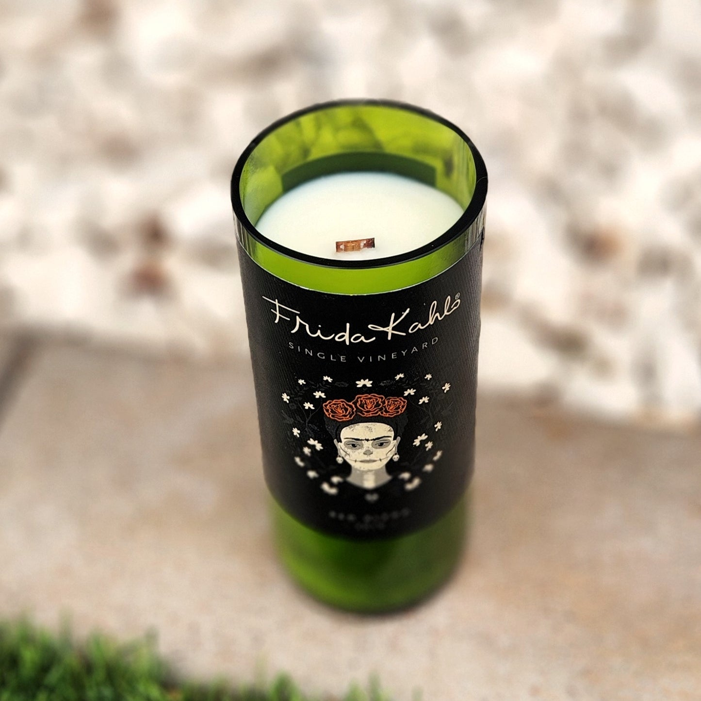 Angled look inside a Frida Kahlo wine bottle candle with white coconut soy wax and a wooden wick, housed in a deep green upcycled glass container with a striking black and floral label.