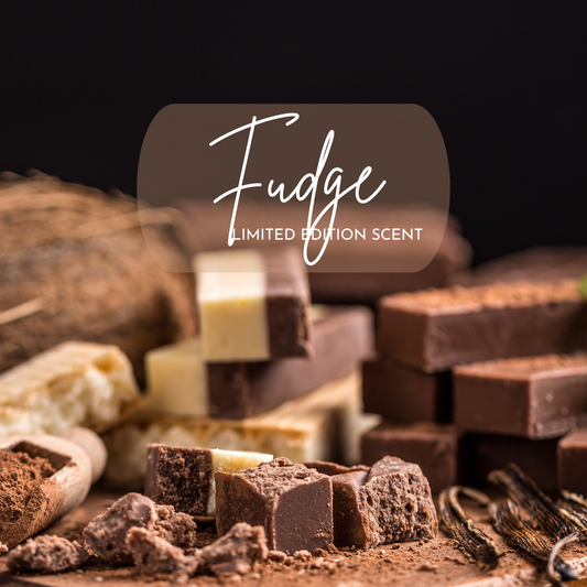 Artistic image showcasing rich chocolate and vanilla fudge pieces on a wooden board, with cocoa powder, crushed chunks, and vanilla beans scattered in the foreground. A translucent label overlay reads “Fudge – Limited Edition Scent,” promoting a decadent, dessert-inspired candle fragrance. Ideal for fall and holiday gift ideas, chocolate lovers, and cozy home decor fans.