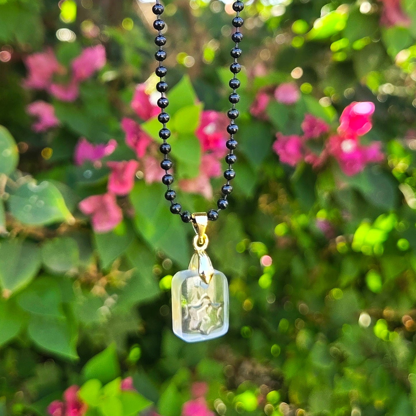 Necklace with a clear glass pendant with raised star hanging against a blurred natural background with pink flowers.