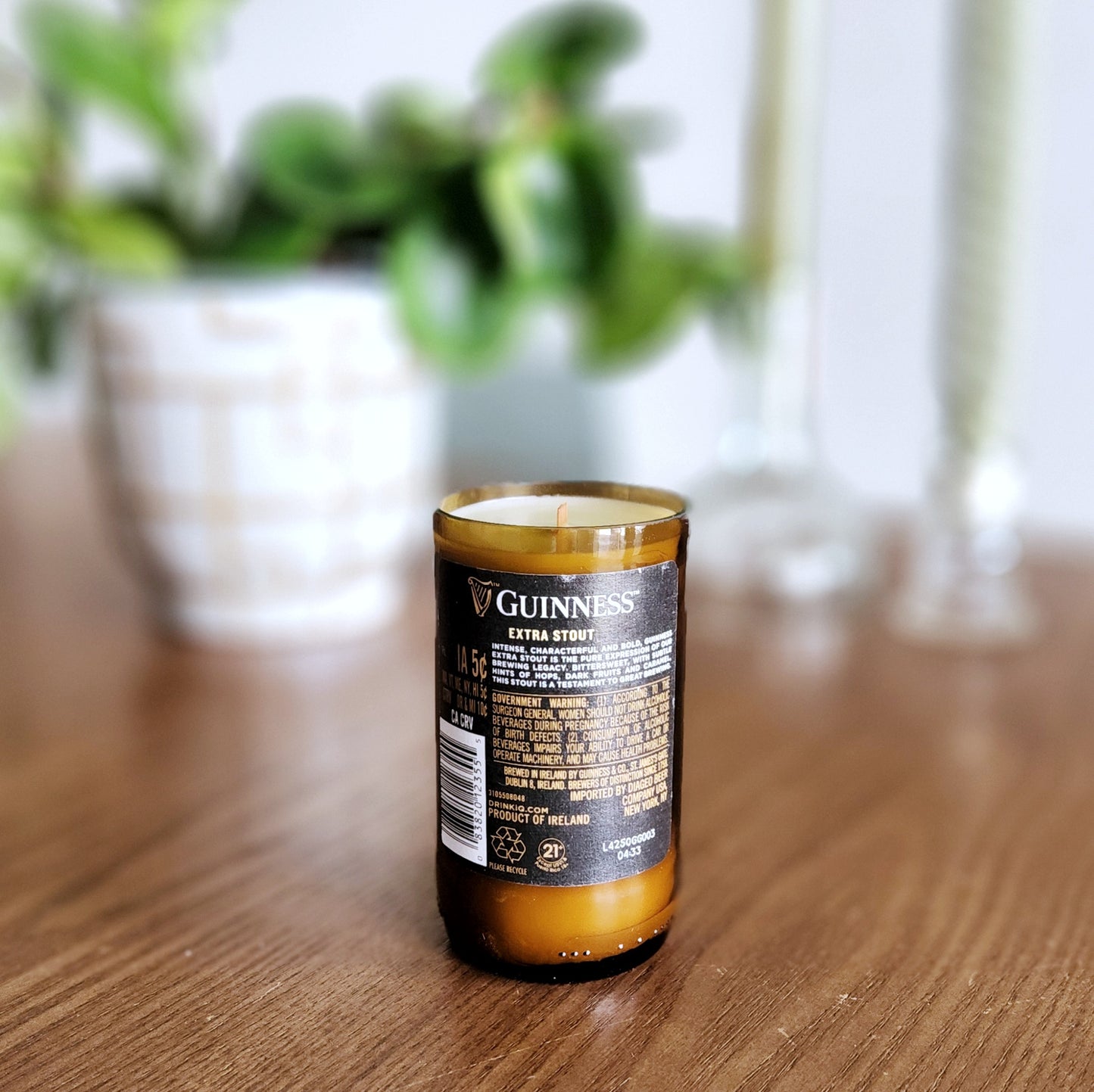 Back view of a recycled Guinness bottle candle featuring the original label and barcode; the amber glass glows warmly around the hand-poured coconut soy wax and wooden wick.