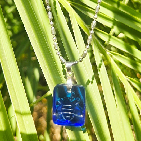Blue glass pendant necklace on a chain against a green leafy background