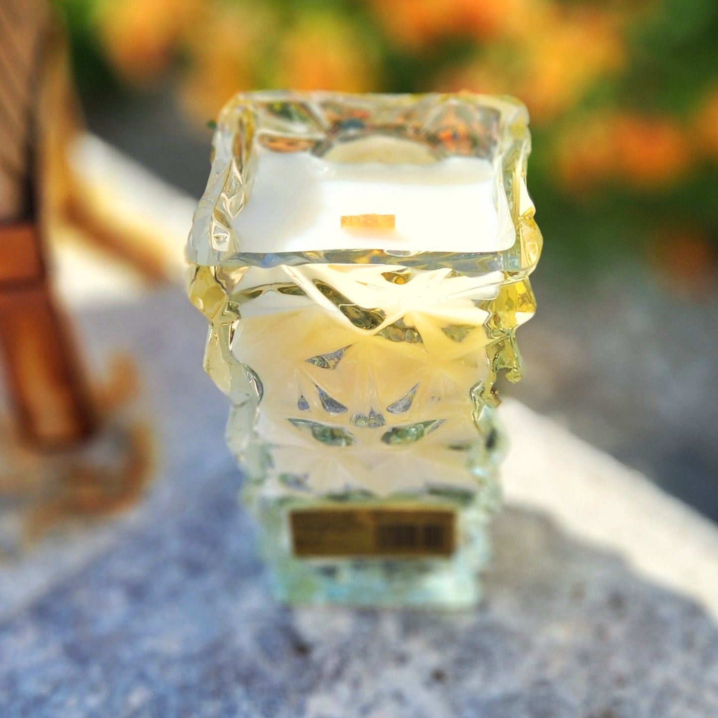 A clean-burning coconut soy candle in an upcycled Mi Familia Flores tequila bottle, showing the textured glass pattern and wooden wick through the wax from an angled side view.