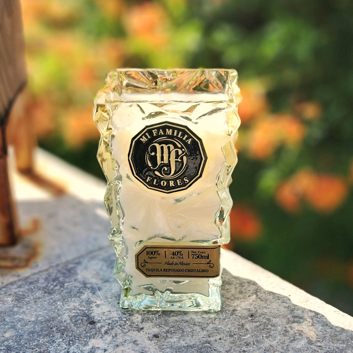 Luxury recycled candle made from a Mi Familia Flores tequila bottle, featuring bold black and gold branding, artisan-cut glass, and filled with eco-friendly coconut soy wax.