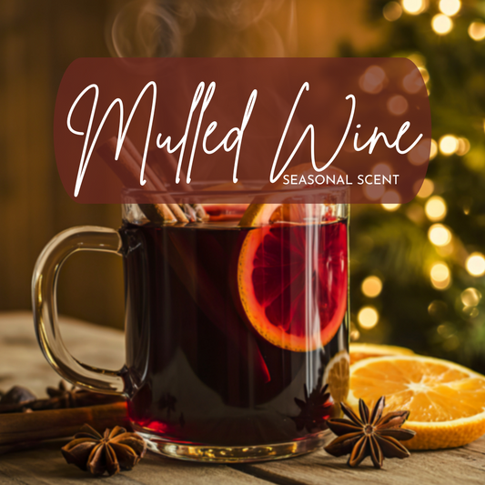 A cozy, holiday-inspired image featuring a clear glass mug filled with steaming mulled wine, garnished with a bright orange slice, cinnamon sticks, and star anise on a rustic wooden table. Warm golden bokeh lights and a softly blurred Christmas tree glow in the background, creating a festive winter atmosphere. Overlay text reads “Mulled Wine – Seasonal Scent,” evoking notes of spiced red wine, citrus peel, and cozy holiday warmth.
