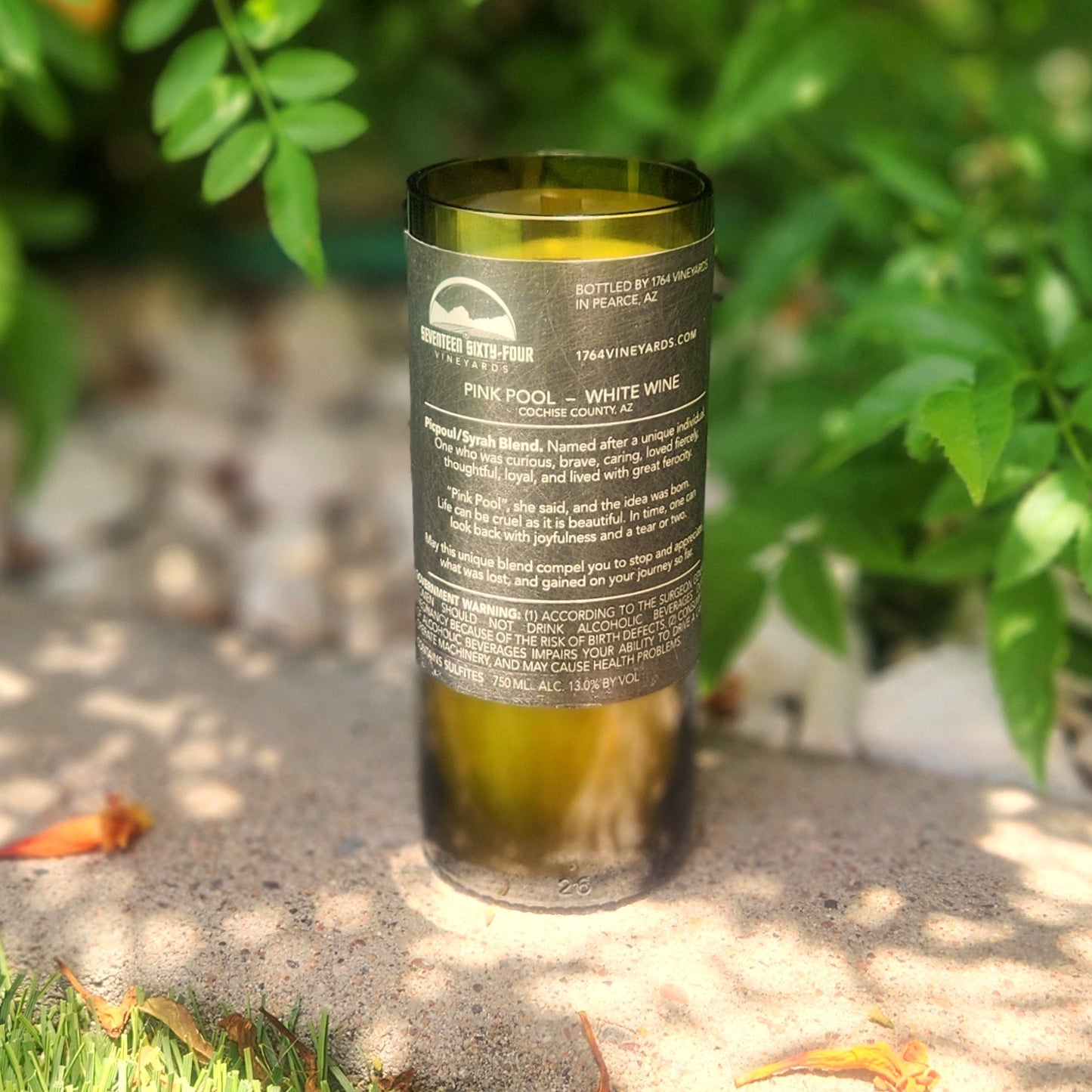 Back label view of a Pink Pool wine bottle candle made from a recycled wine bottle, featuring a clean-burning coconut soy wax blend and eco-friendly wooden wick. Text details the white wine origin and sentimental vineyard story, ideal for Arizona wine lovers seeking unique home décor.