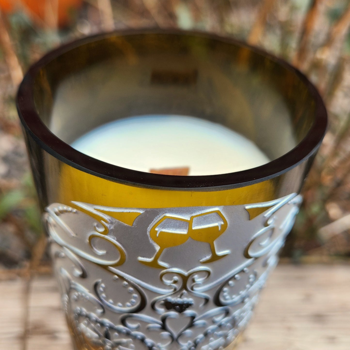 Close-up of a handmade wine bottle candle with a glossy smooth rim, wooden wick, and elegant sugar skull and filigree etching, made from a recycled wine bottle.