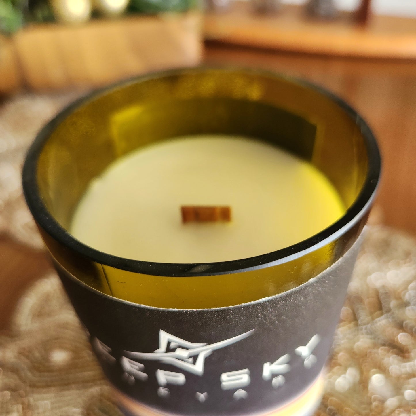 Close-up angled view of a clean-burning Comet wine bottle candle inside a recycled Deep Sky Vineyard bottle, showcasing the natural wooden wick and smooth rim. The sleek label and golden-green glass give it a refined, handcrafted look. Coconut soy wax blend.