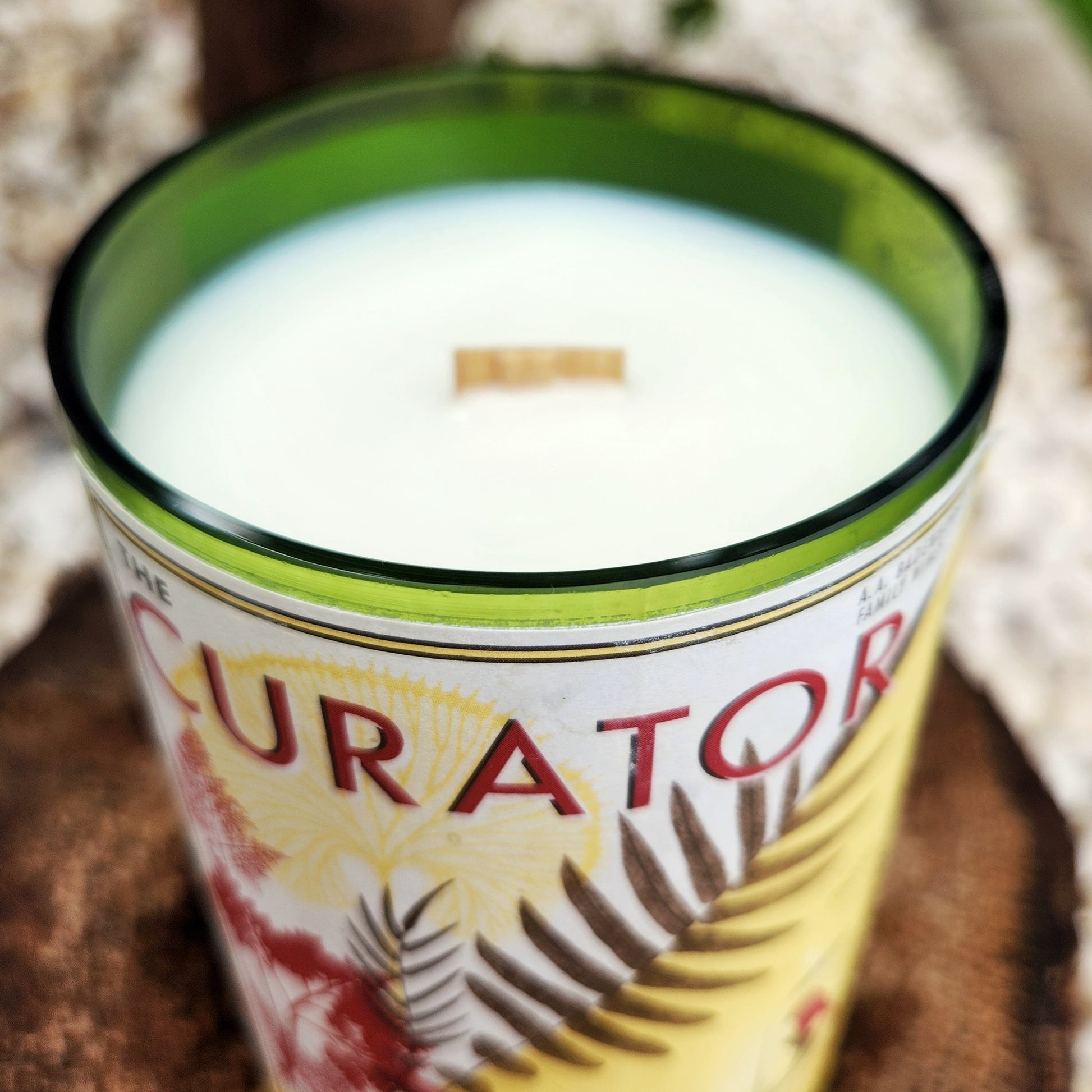Close-up of the smooth glass rim and wooden wick of a handmade wine bottle candle with the Curator label, showcasing sustainable coconut soy wax.