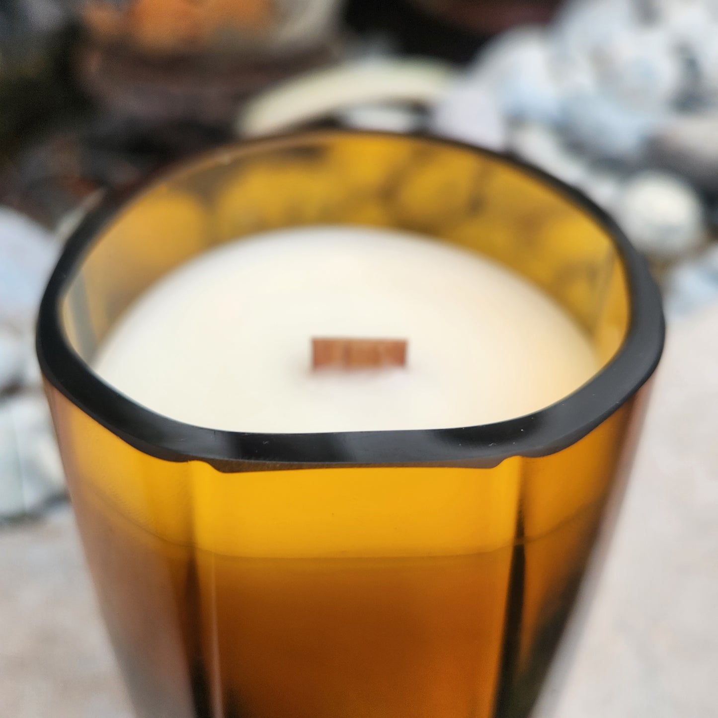 Close-up of a clean-cut rim and wooden wick in a sustainable coconut soy candle housed in an amber upcycled bottle, ideal for eco-conscious decor.