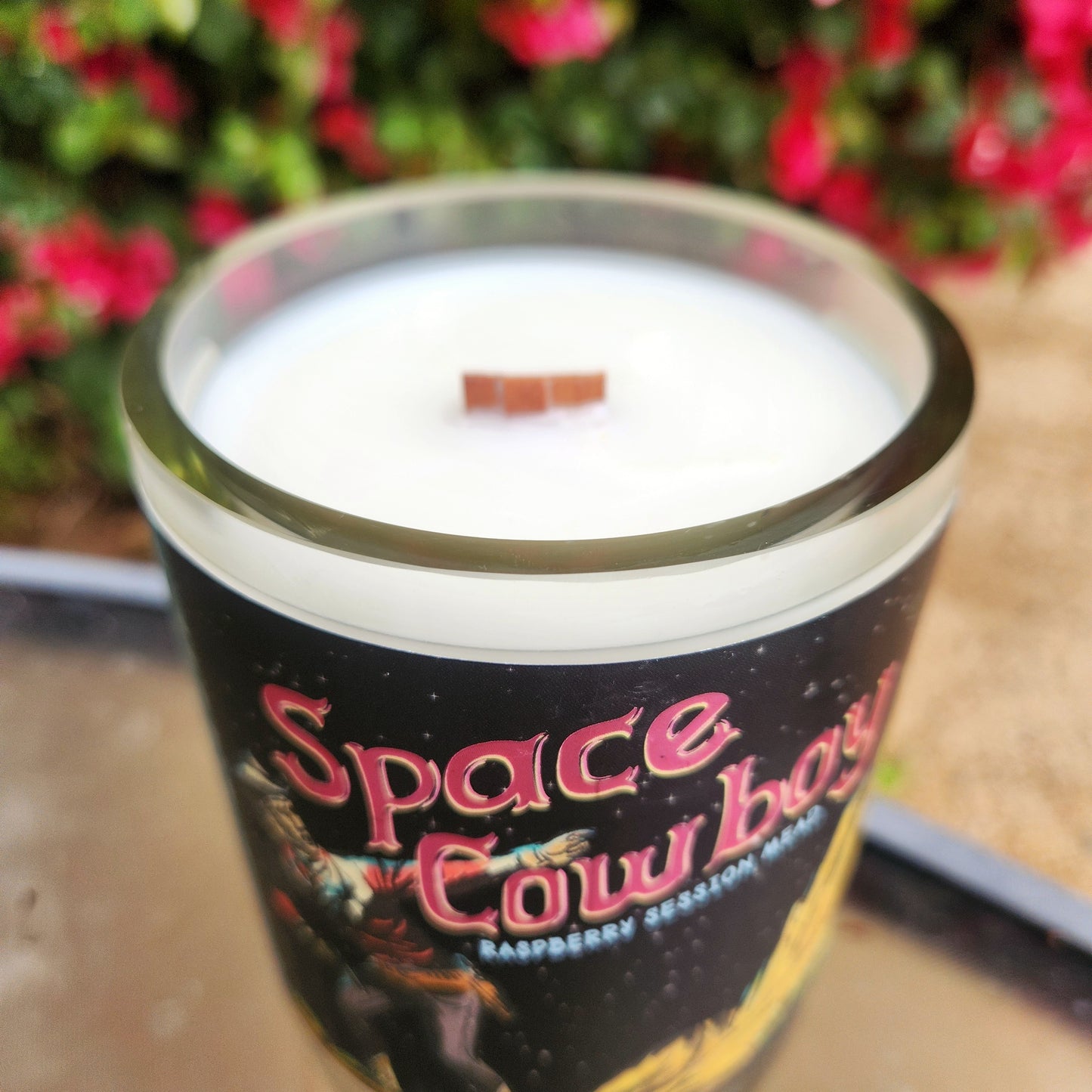 A clean-burning wooden wick candle made from a recycled mead bottle, featuring an eco-friendly design with the "Space Cowboy" raspberry mead label and a smooth glass rim.