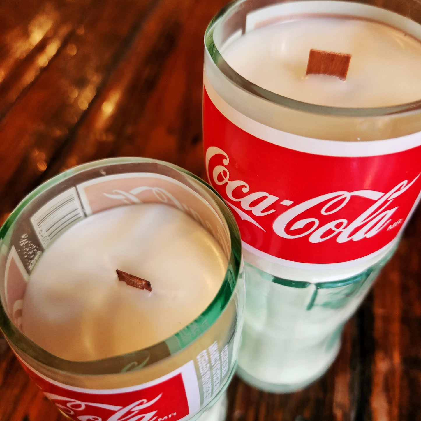 Close-up of the smooth rim edges and wooden wicks of two eco-friendly Coca-Cola bottle candles. These recycled glass vessels are hand poured with coconut soy wax for a non-toxic, clean burn.