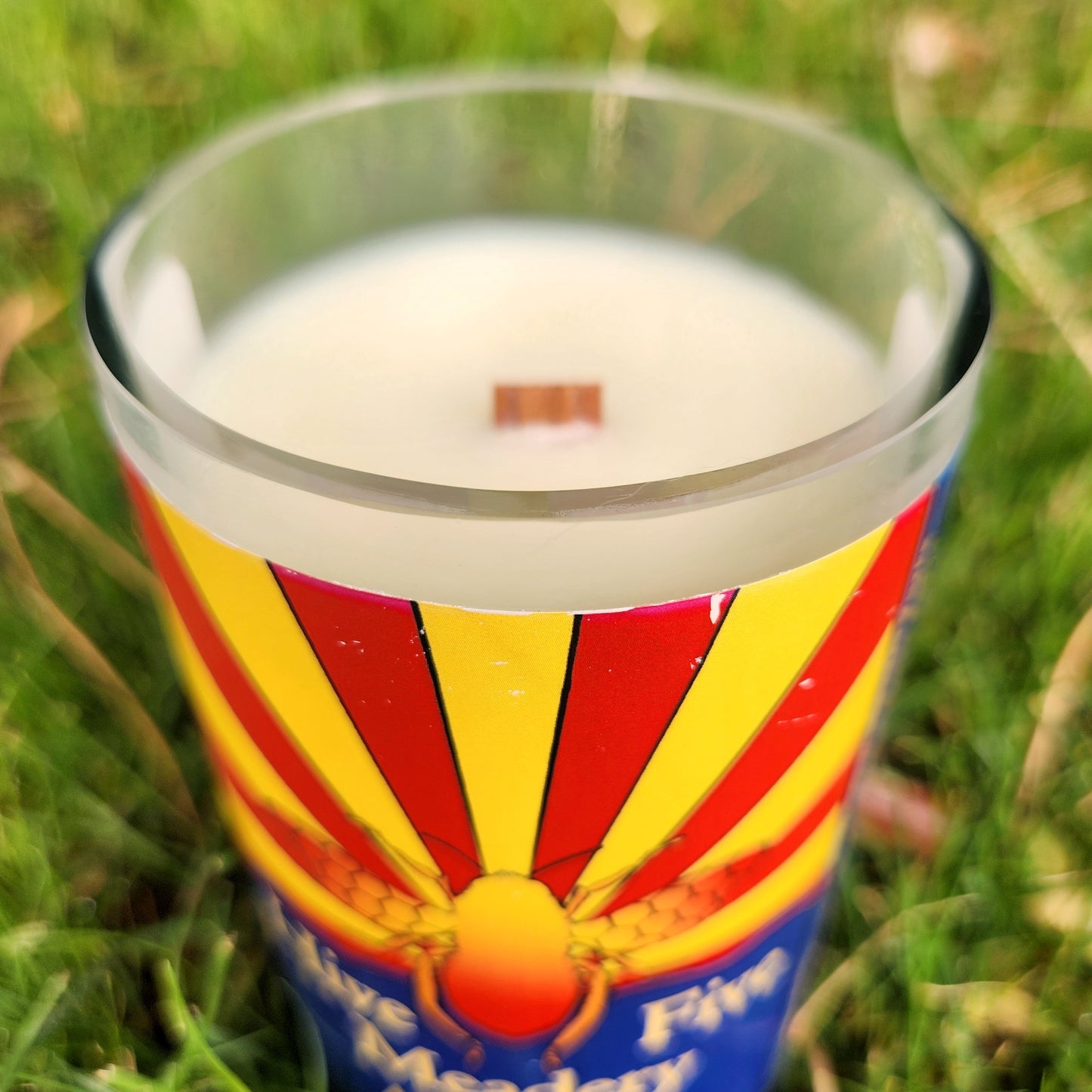 Close-up of the smooth glass rim and wooden wick of a handcrafted candle made from a repurposed Hive Five Meadery bottle featuring the Arizona state flag.
