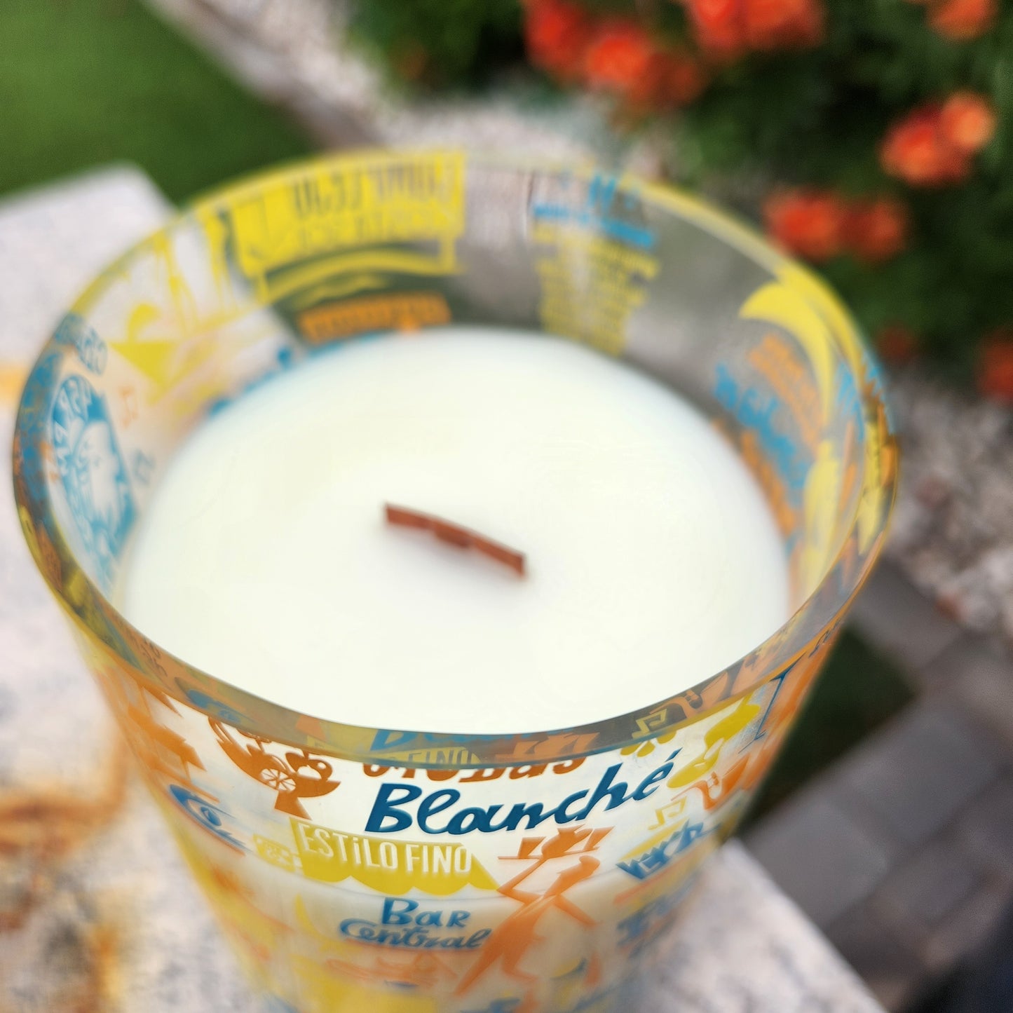 Close-up of the rim of a recycled wine bottle candle with a colorful travel-themed label; smooth, shiny edge reveals the clean white wax and centered wooden wick inside.
