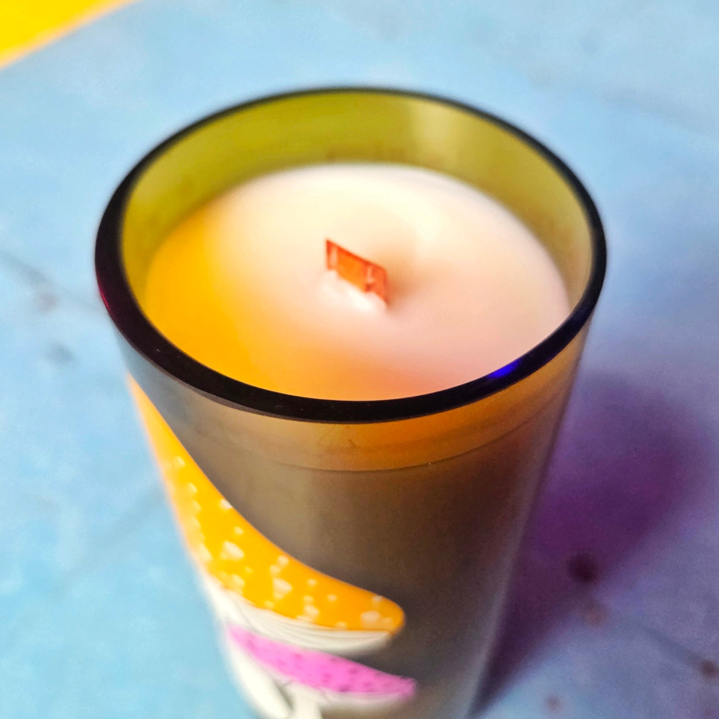 Close-up of the smooth coconut soy wax surface inside a recycled bottle candle. The shiny rim and centered wooden wick highlight the clean craftsmanship and eco-conscious design.