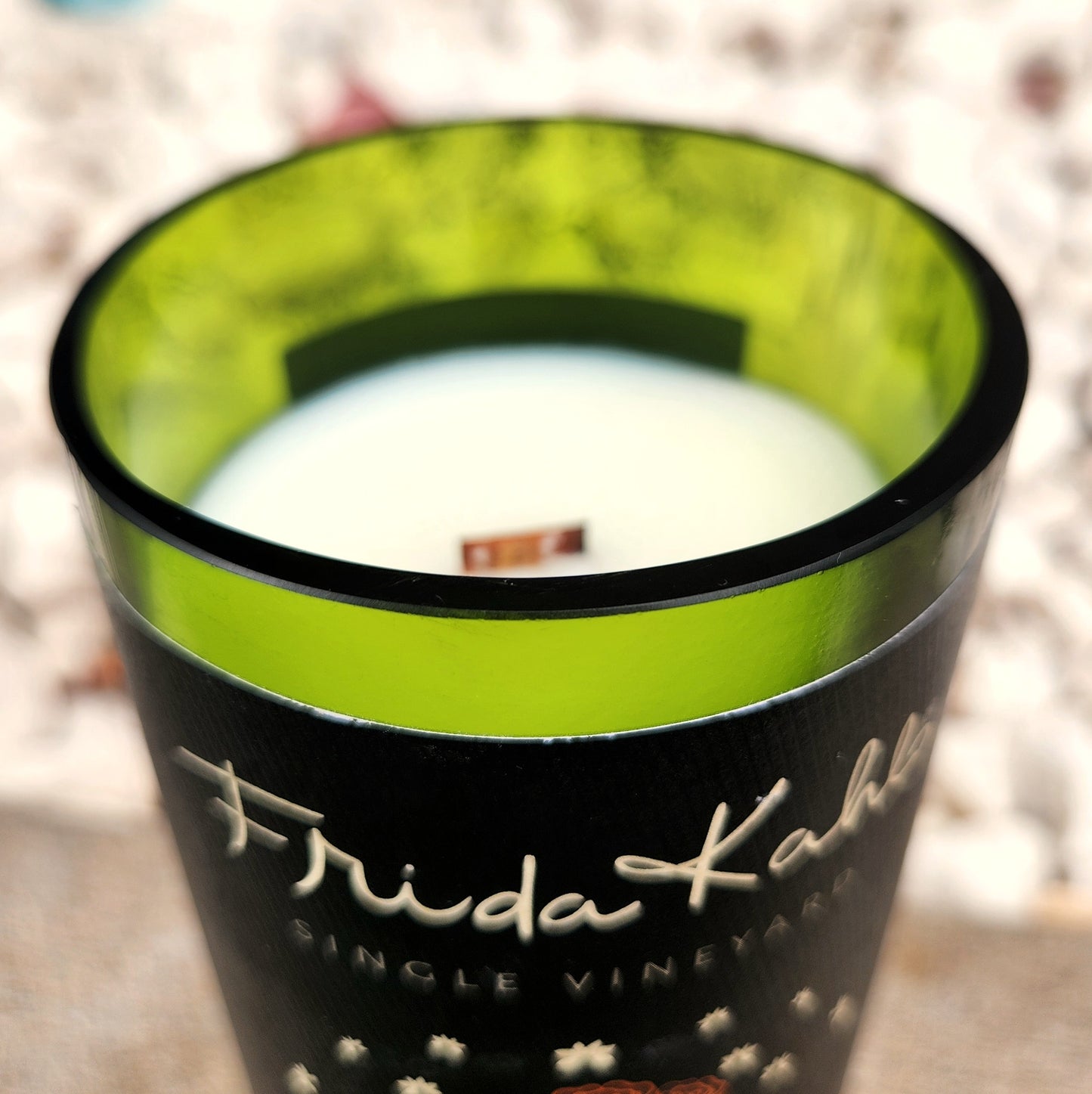 Close-up of the wooden wick and smooth rim of a repurposed Frida Kahlo wine bottle candle, showcasing the vibrant green interior and eco-friendly coconut soy wax pour.
