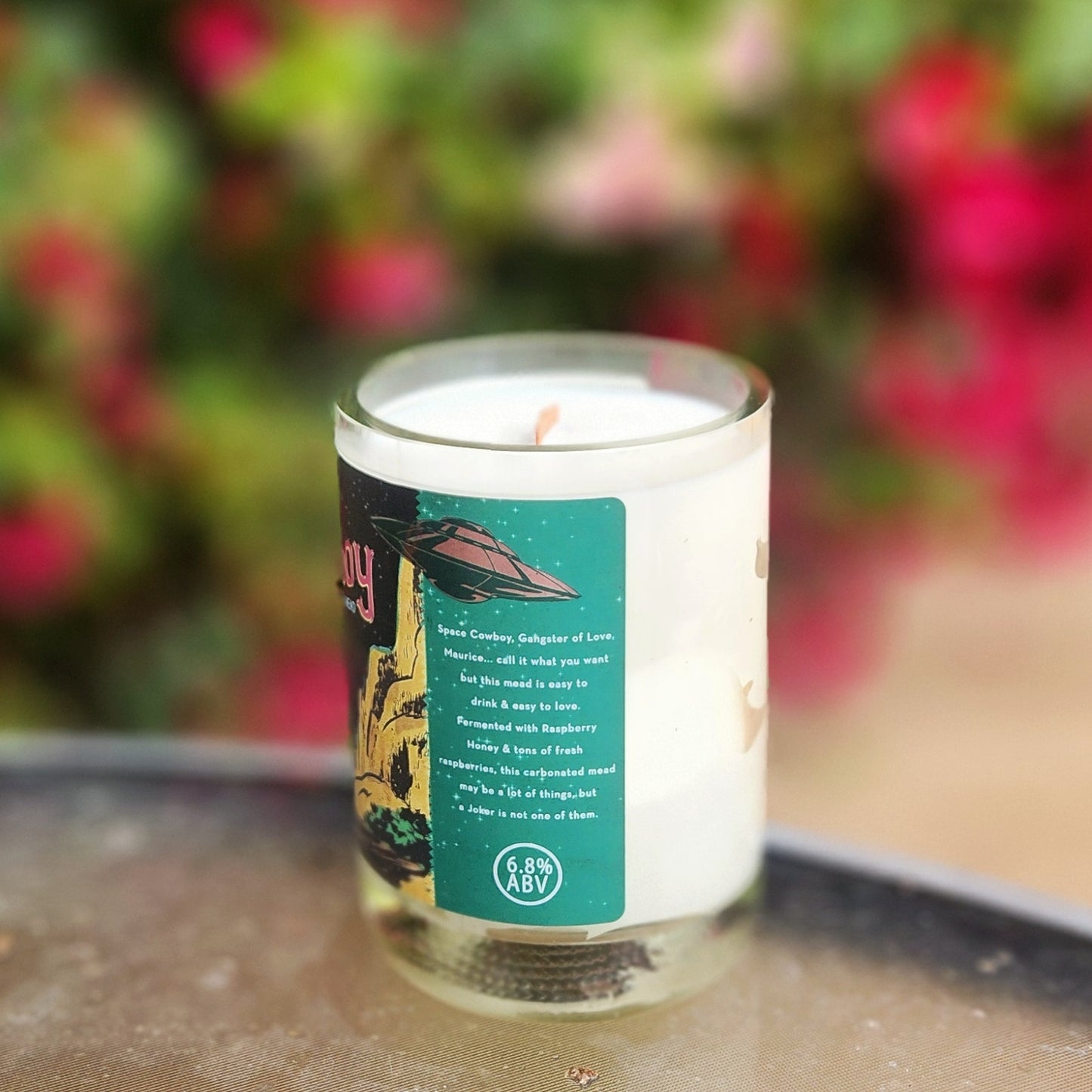 A clean-burning wooden wick candle made from a recycled mead bottle, featuring an eco-friendly design with the "Space Cowboy" raspberry mead label and a smooth glass rim.