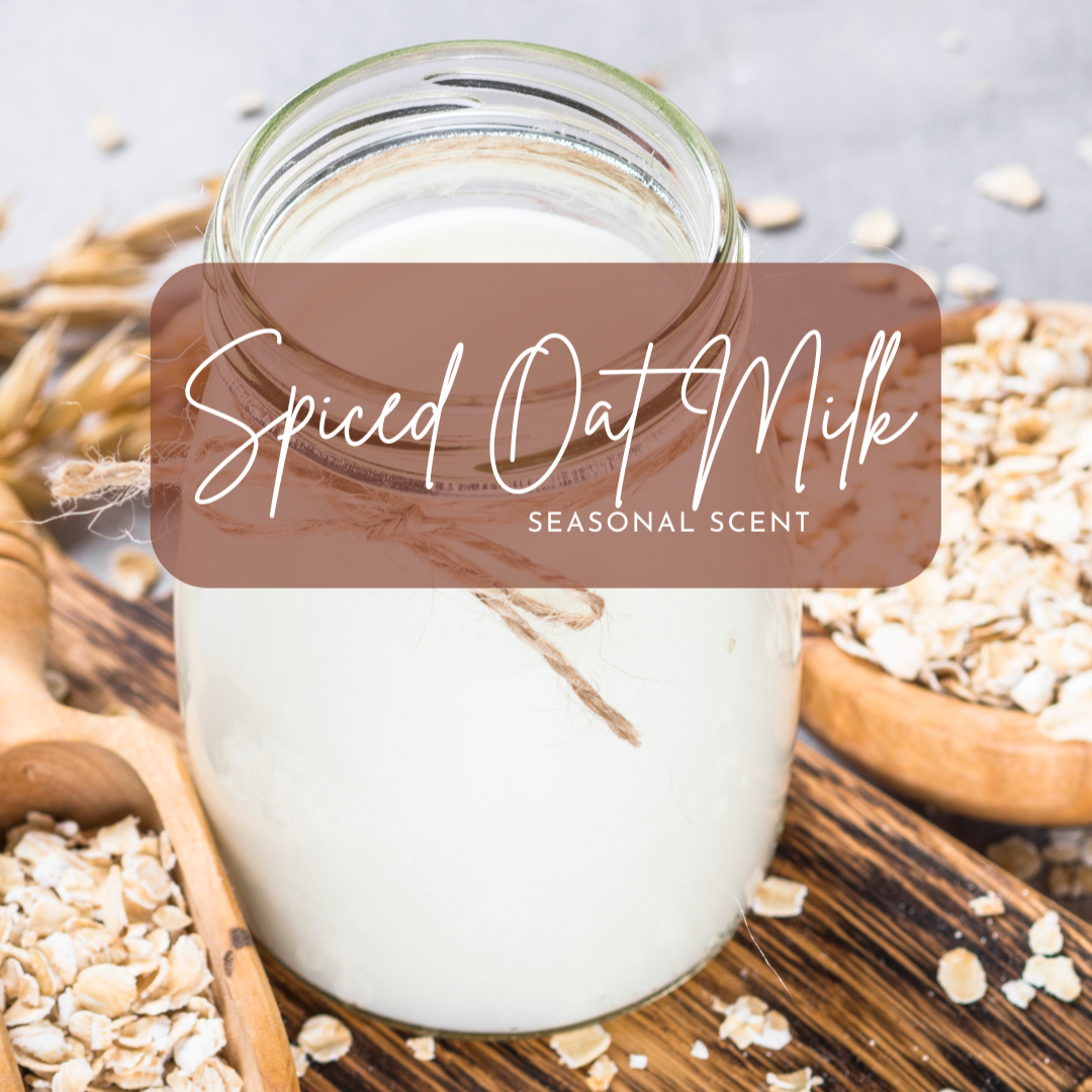 A rustic jar of creamy oat milk tied with twine sits on a wooden board surrounded by rolled oats and grain stalks, promoting the Spiced Oat Milk seasonal scent—warm, cozy, and subtly sweet.