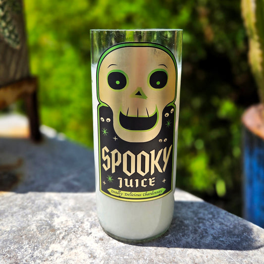 Front-facing view of a Spooky Juice wine bottle candle, featuring a grinning green skull graphic and gothic-style lettering. Crafted from a recycled wine bottle, this coconut soy wax candle includes a wooden wick for a clean-burning finish.