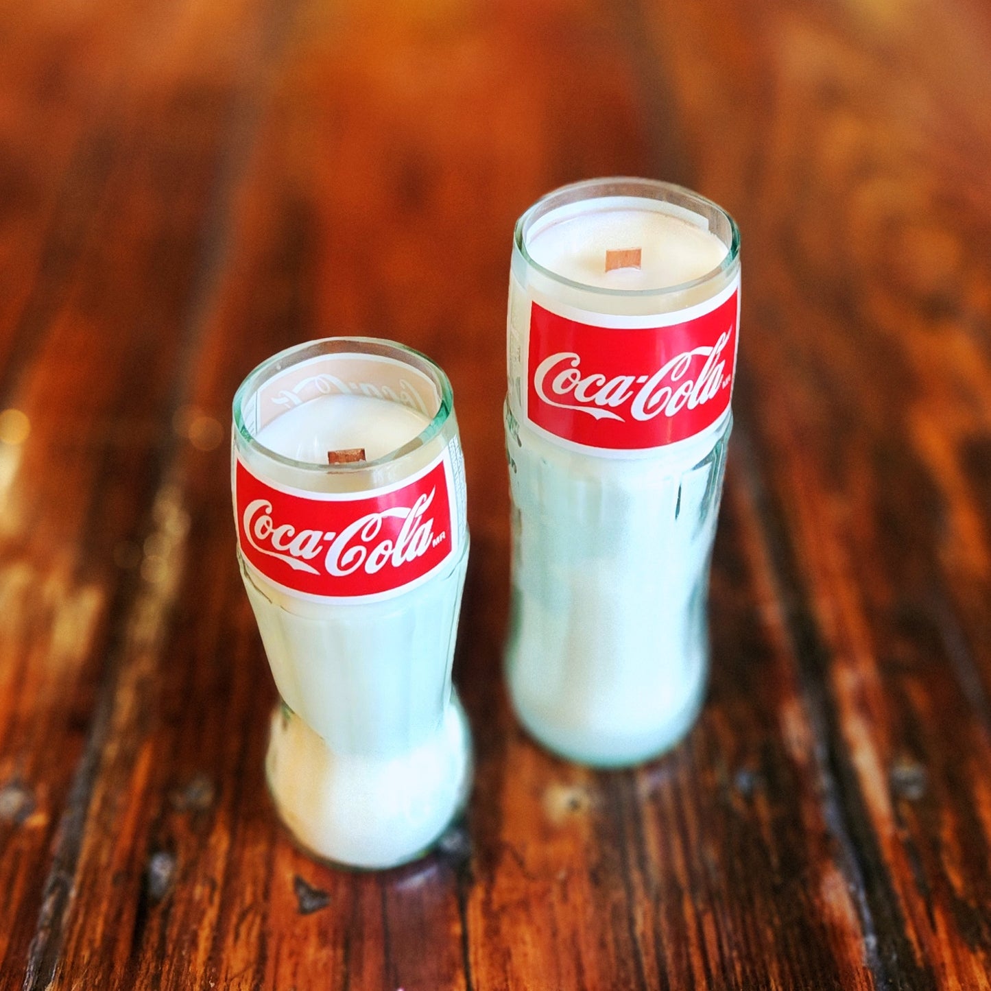 Angled top view of two clean-burning candles with wooden wicks, crafted in repurposed Coca-Cola glass bottles and filled with creamy white coconut soy wax.