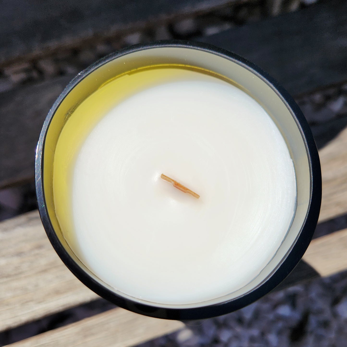 Top-down view of a clean-burning wooden wick wine bottle candle. The creamy coconut soy wax is smooth and even, poured into a recycled glass vessel with a bright yellow inner rim for added character