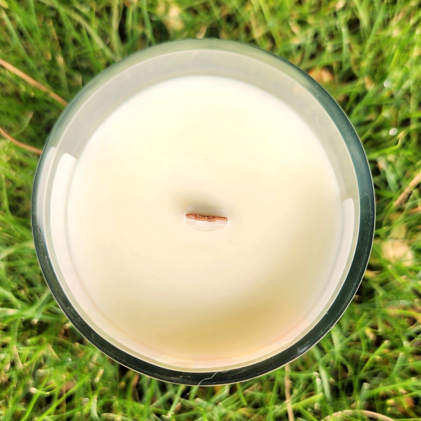 Top view of a clean-burning coconut soy wax candle with a wooden wick, hand-poured into a recycled Arizona mead bottle and surrounded by grass.