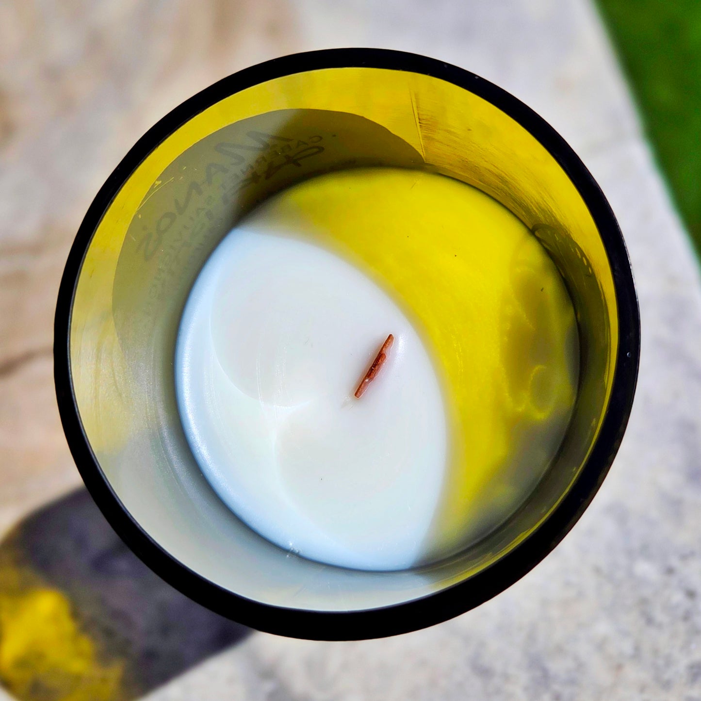 Top-down view of a hand-poured coconut soy wax wine bottle candle with a crackling wooden wick, housed in a recycled bottle with a smooth glass rim and faint yellow tint, highlighting the clean eco-friendly burn.