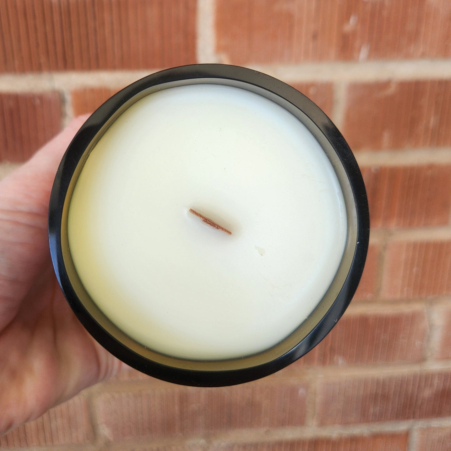 Top view of a hand-poured coconut soy wine bottle candle with a wooden wick. The smooth wax surface and shiny glass rim reflect the natural sunlight, emphasizing its clean-burning, non-toxic quality.