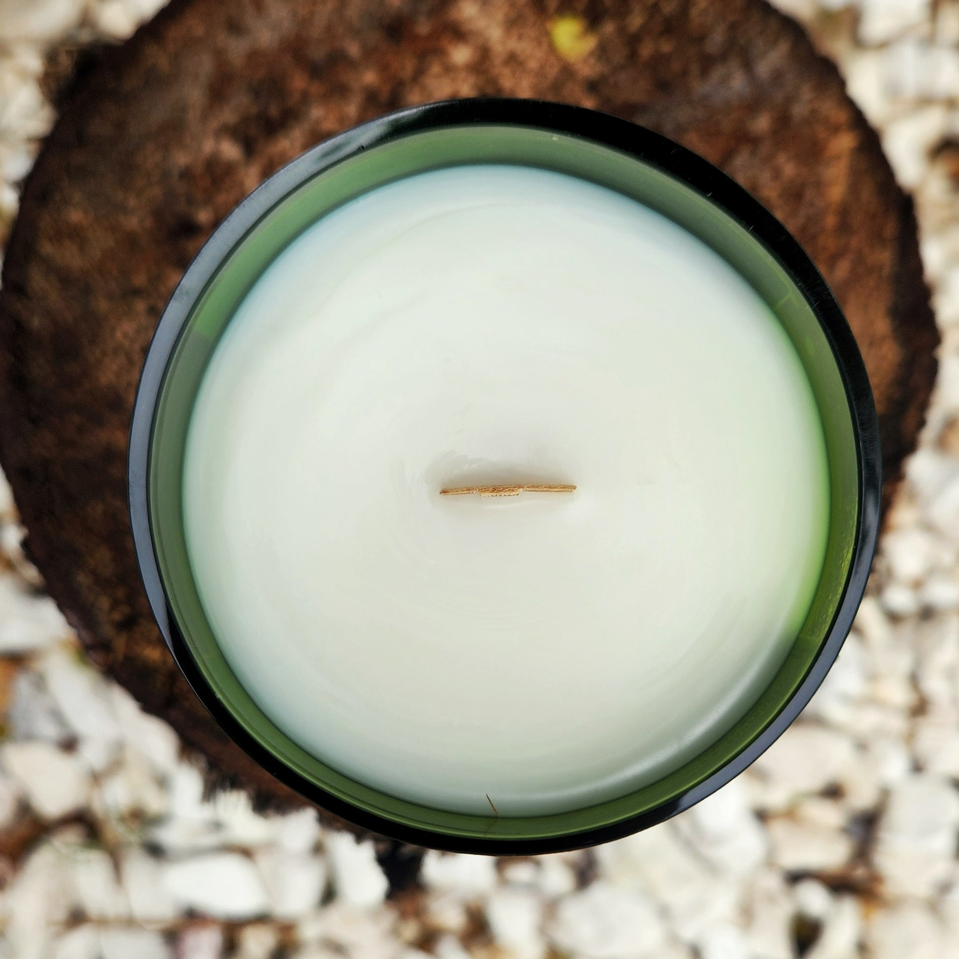 Top-down view of an eco-friendly coconut soy wax candle with a wooden wick, hand poured into a recycled green wine bottle featuring the Curator wine label.