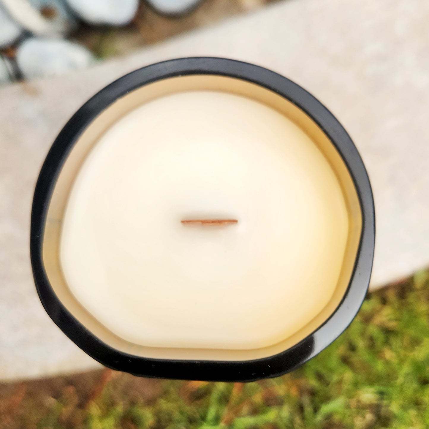 Top view of an eco-friendly candle made from a repurposed liquor bottle, featuring creamy coconut soy wax and a wooden wick for a non-toxic burn.