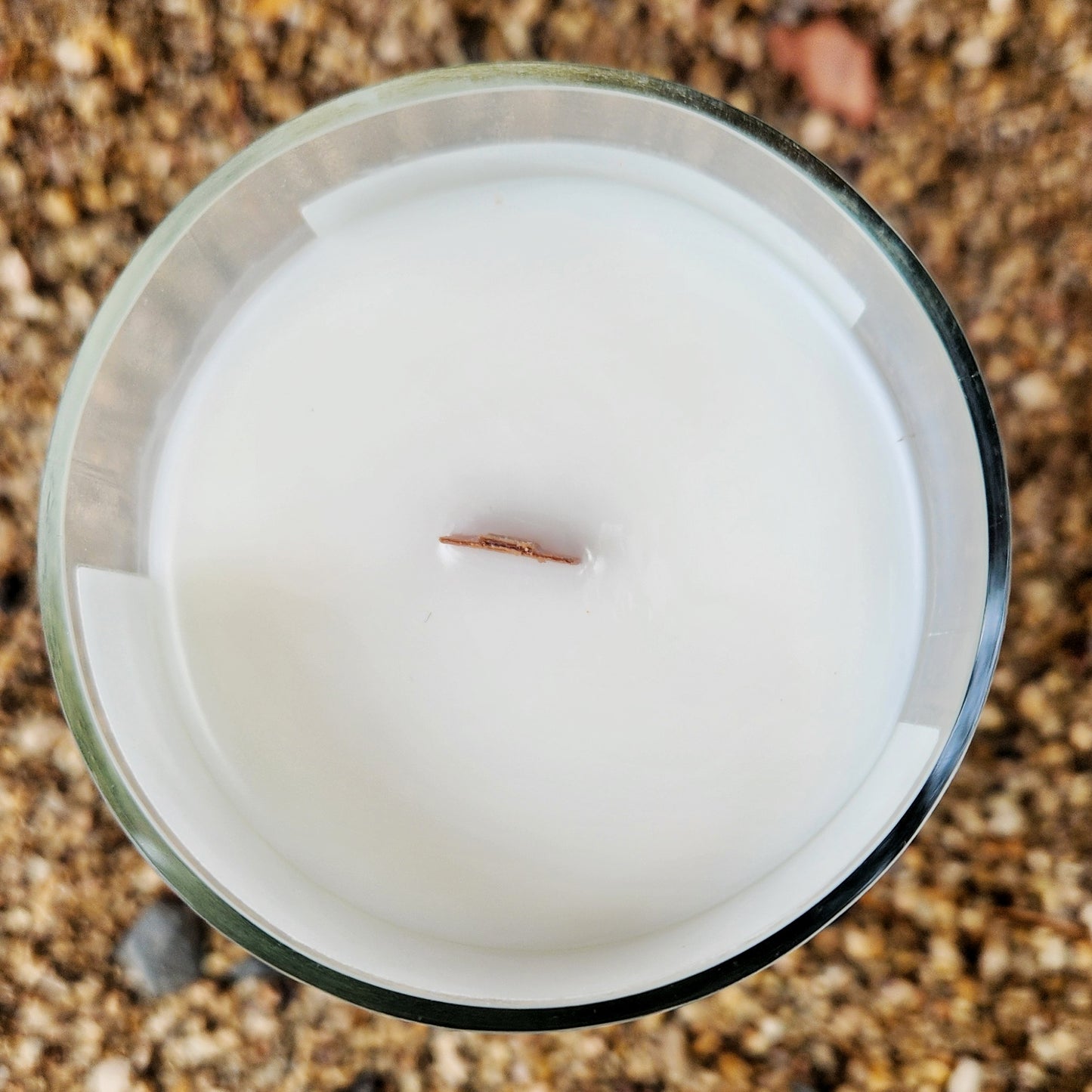 Top-down view of a hand-poured, non-toxic candle with a wooden wick nestled in creamy coconut soy wax. The smooth, shiny glass rim reflects natural light, emphasizing the sustainable craftsmanship of this recycled wine bottle candle.