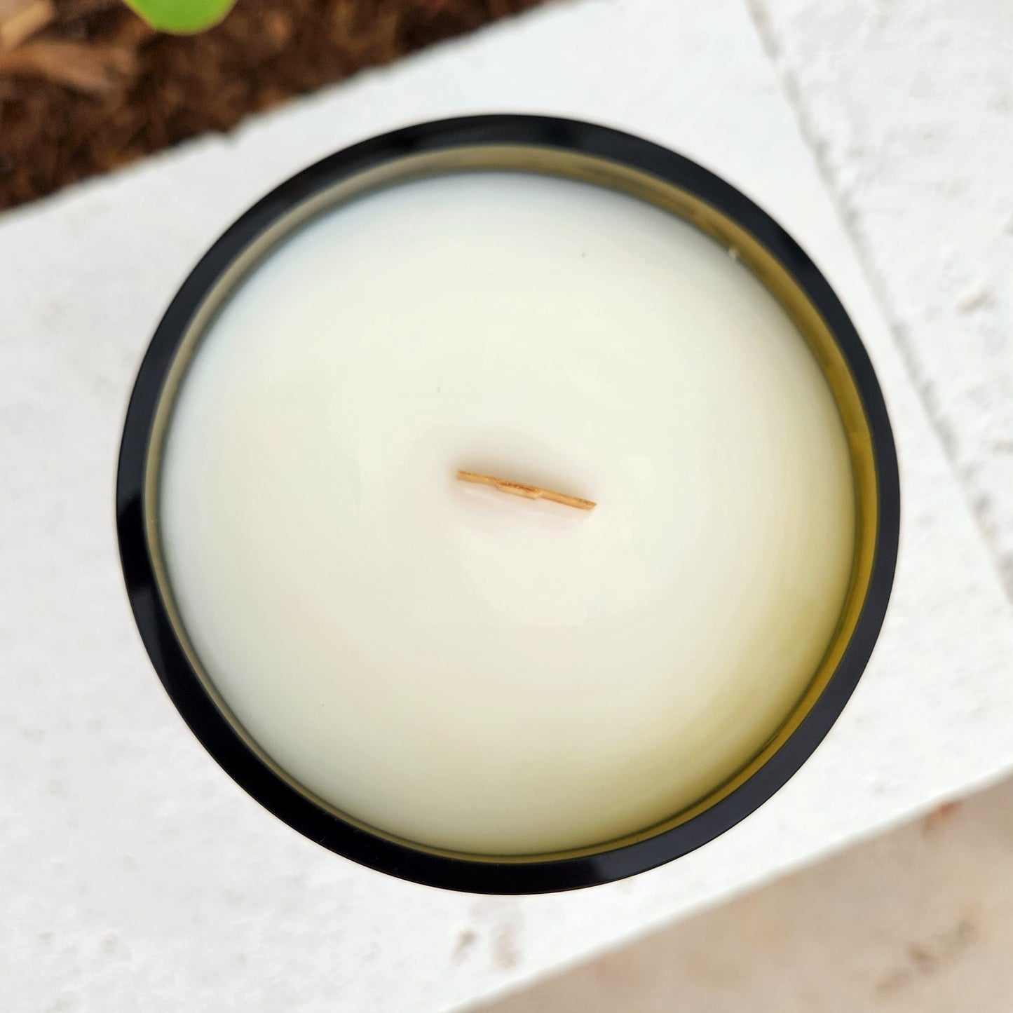 A clean-burning, hand-poured candle made with coconut soy wax and a centered wooden wick, housed in a glossy recycled green wine bottle with a smooth rim—captured from above for a crisp, minimal aesthetic.