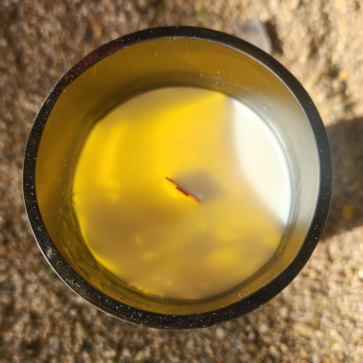 Top-down view of a clean-burning, non-toxic candle with a centered wooden wick and creamy coconut soy wax, housed in an amber recycled wine bottle with a polished smooth rim.