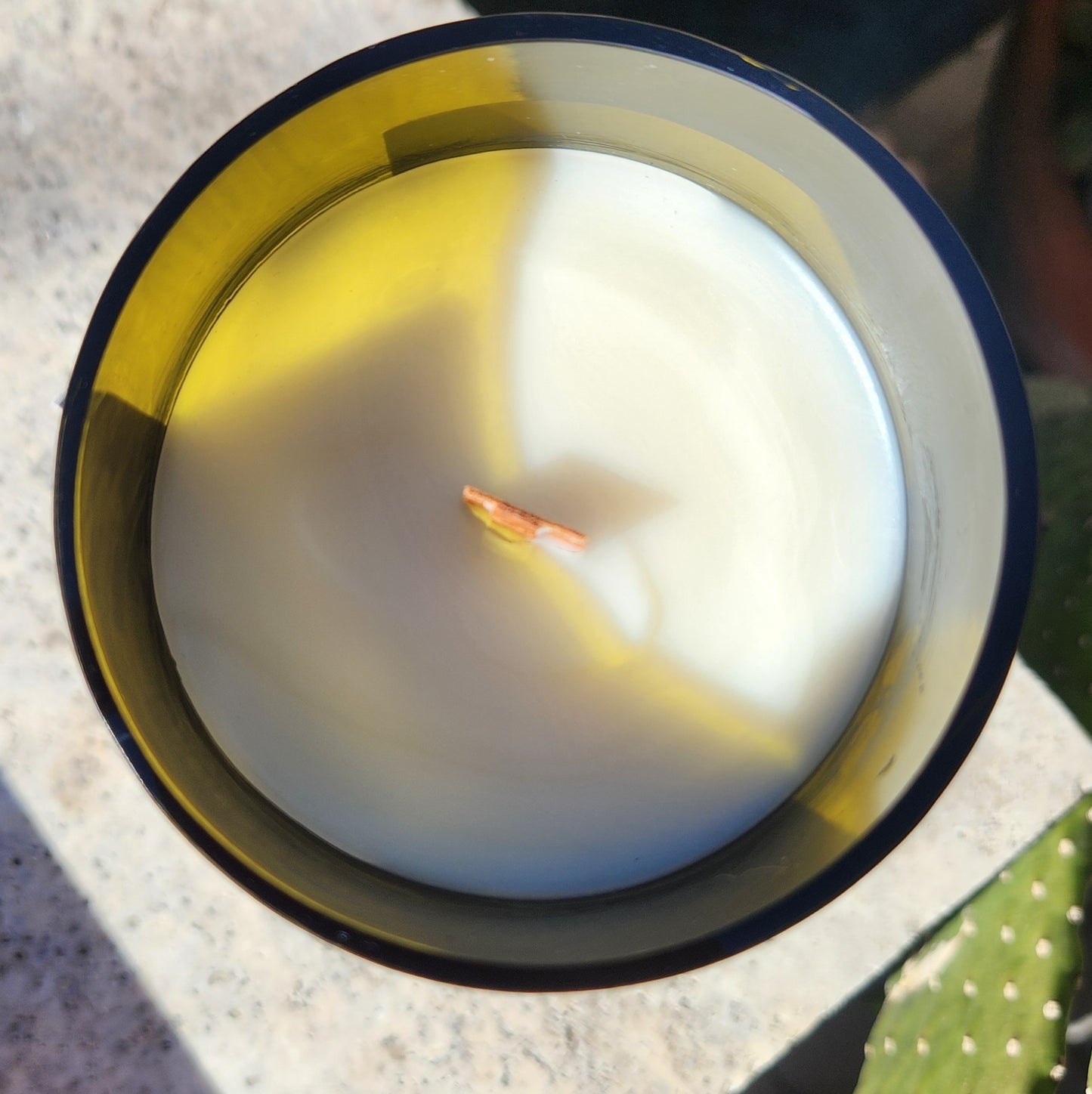 Top view of recycled bottle candle with clean coconut soy wax and a centered wooden wick on a stone surface