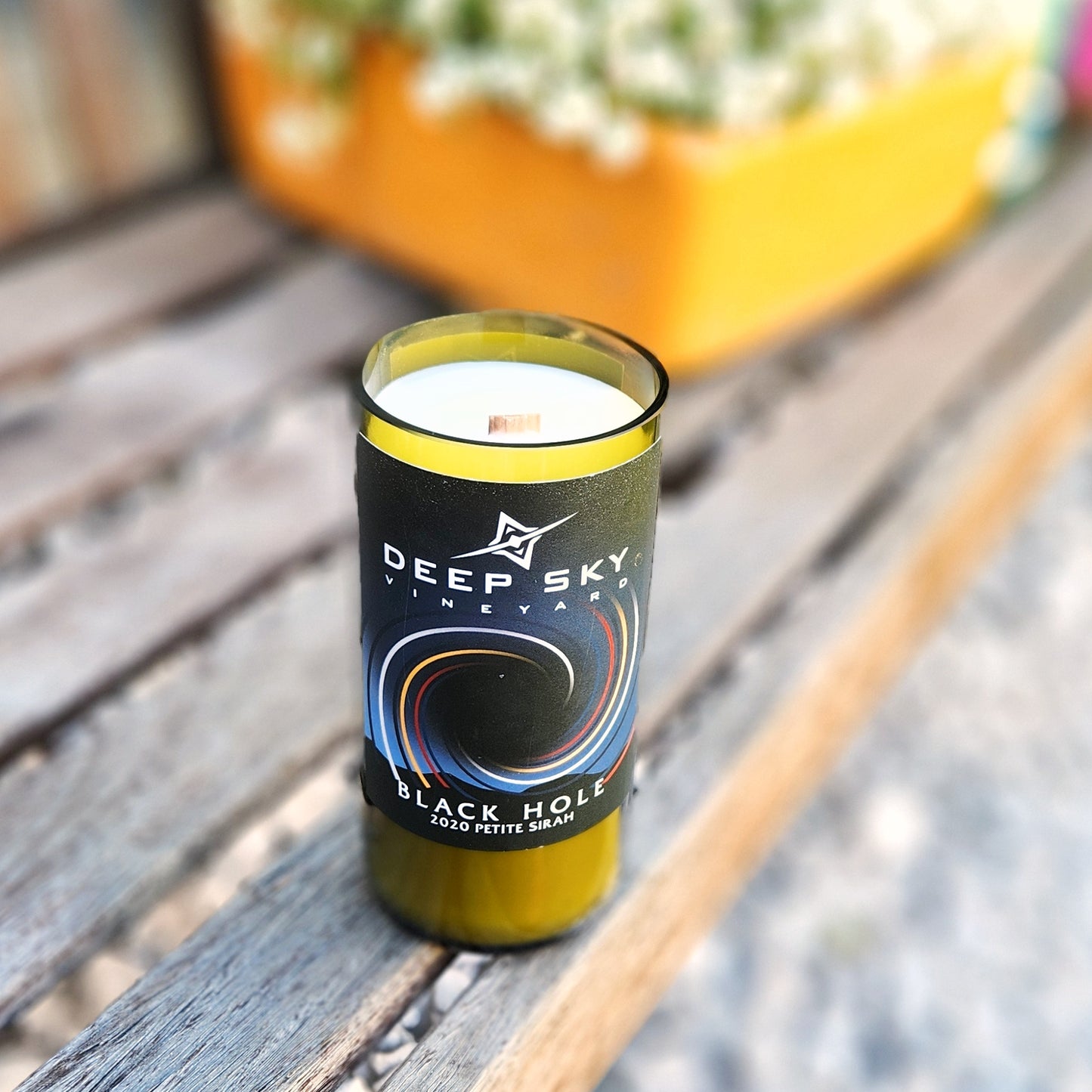 Angled shot of a handmade candle poured into a Deep Sky Vineyard “Black Hole” wine bottle. The vibrant label and shiny glass rim highlight the repurposed design and artisan quality.