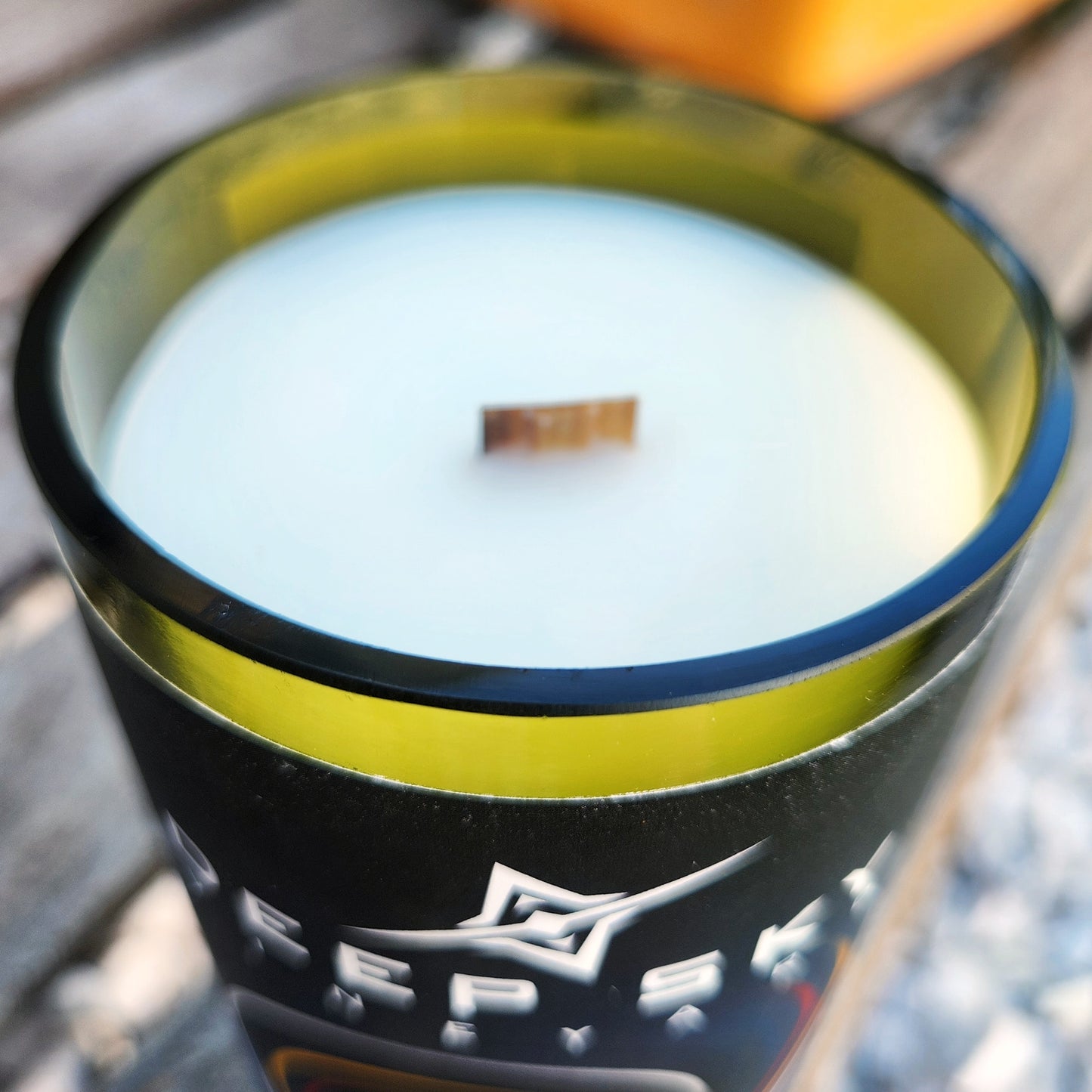 Close-up of the smooth green glass rim and wooden wick of a hand poured candle in a recycled Deep Sky Vineyard “Black Hole” bottle. The creamy wax contrasts with the bottle’s bold black label.