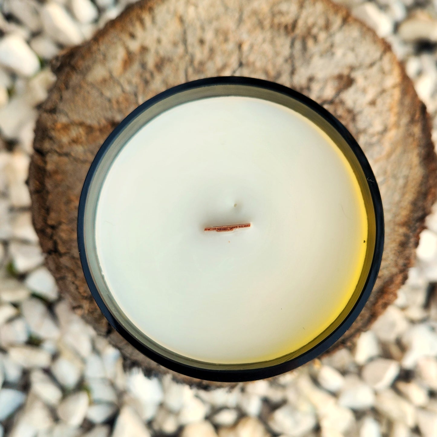 Top-down view of a clean-burning wine bottle candle, filled with creamy white coconut soy wax and centered with a wooden wick. The dark glass rim is smoothly finished and reflects natural outdoor light.