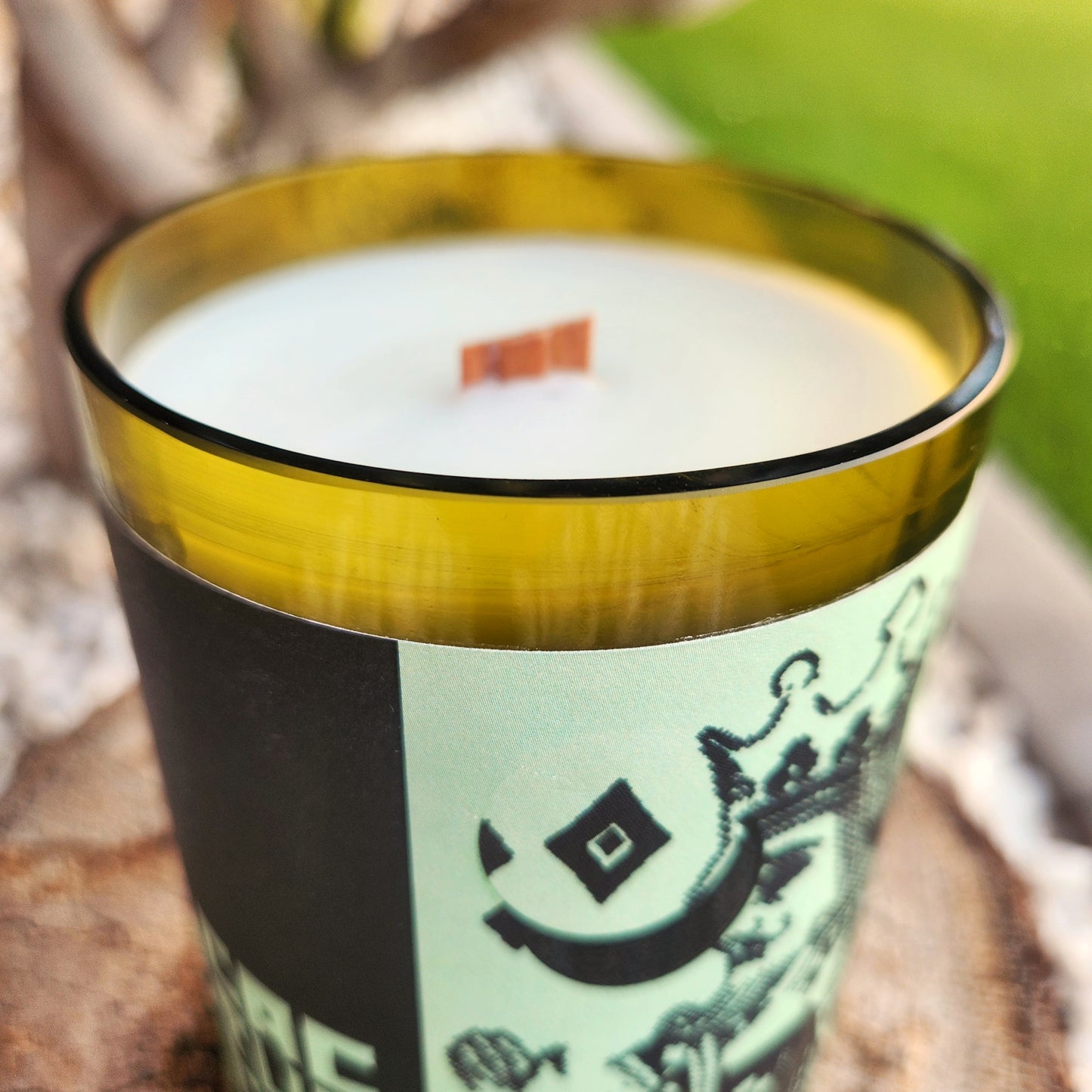 Close-up of a coconut soy wine bottle candle with a shiny, smooth glass rim and wooden wick, emphasizing the detailed recycled label with crown and diamond imagery from a playing card design.
