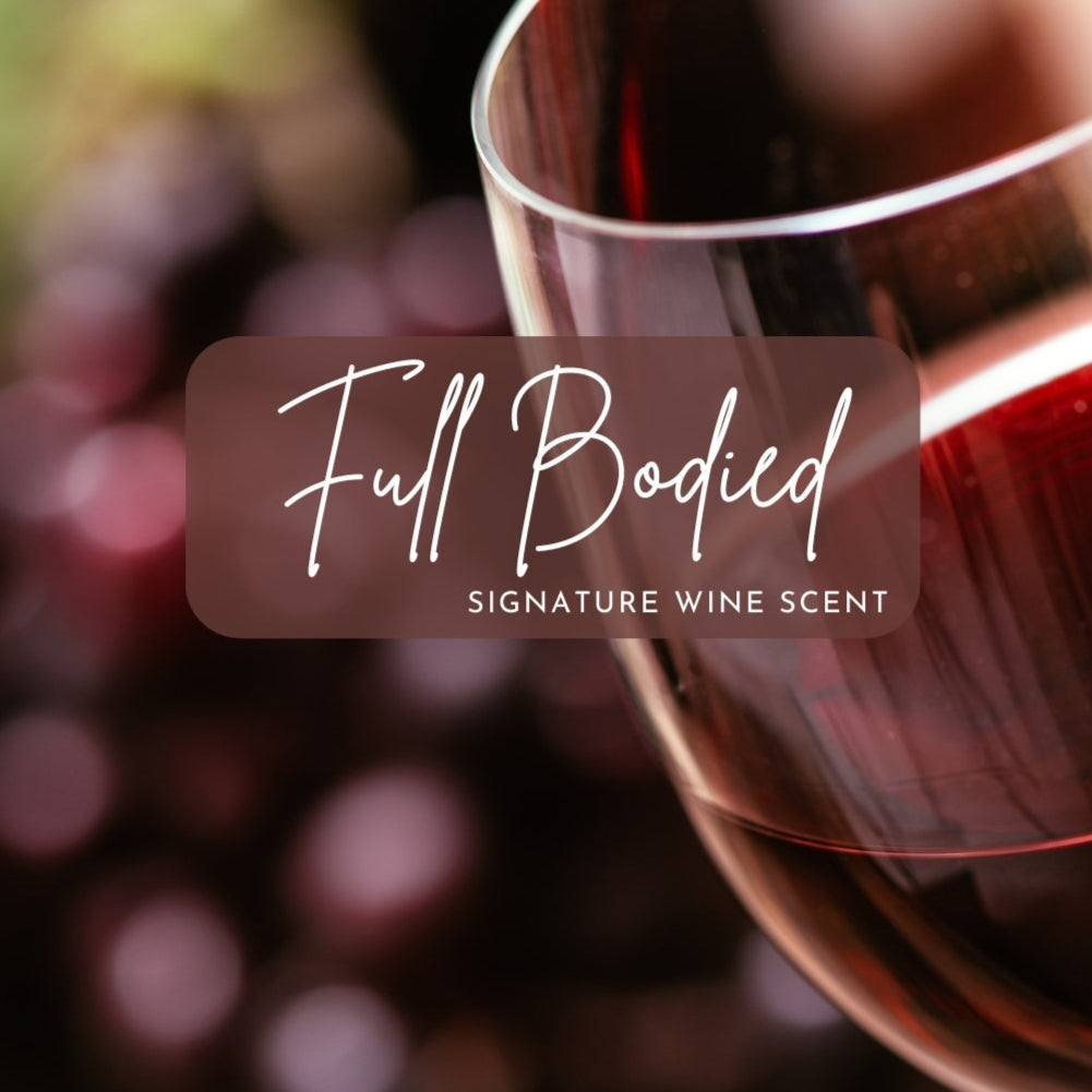 A close-up of a glass of red wine tilted slightly, with a blurred background of plump red grapes. Overlaid text reads “Full Bodied – Signature Wine Scent” in elegant white script, evoking richness and depth.