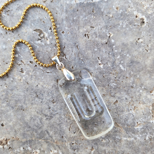 Close-up of Letter U initial necklace made from clear recycled bourbon bottle glass with original raised lettering