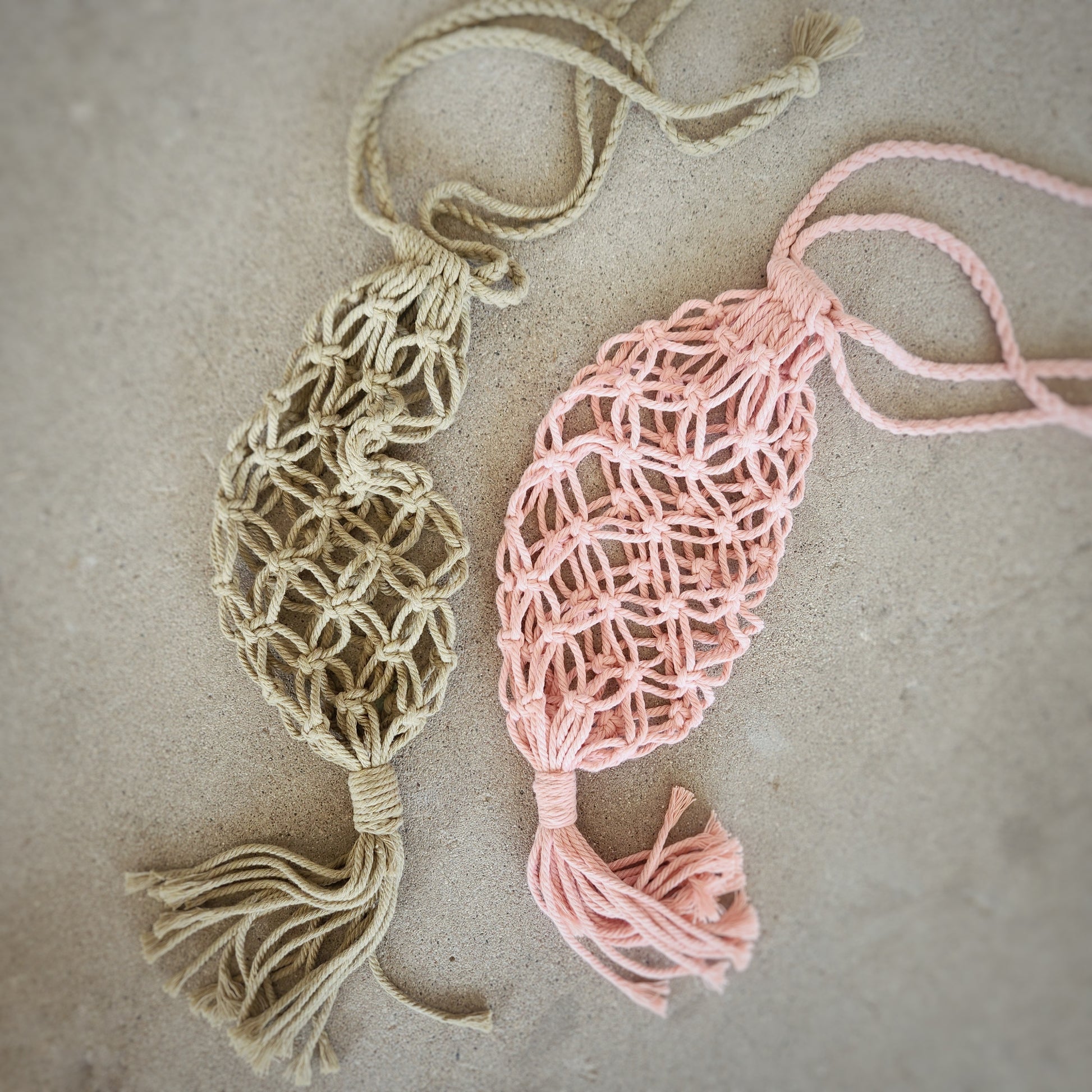 Flat lay of two macrame wine bottle tote bags on a concrete surface, highlighting the unique knot patterns and boho design